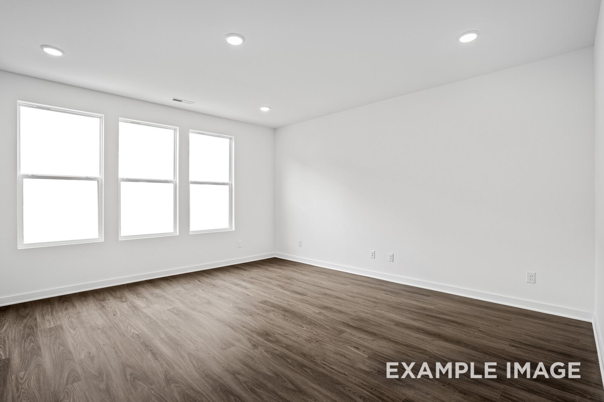 Spacious empty bedroom in The Logan C with white walls, three large windows, recessed lights, and hardwood floors