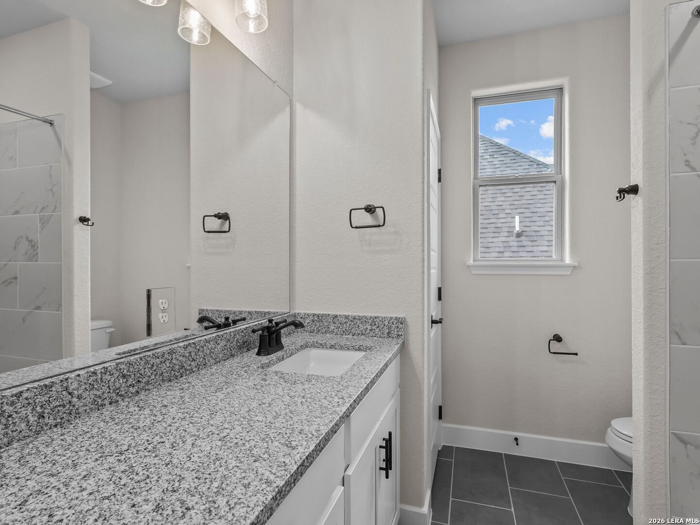 Modern bathroom with granite vanity, dark fixtures, and tiled walk-in shower in a Davidson Homes Belmont H in Castroville.