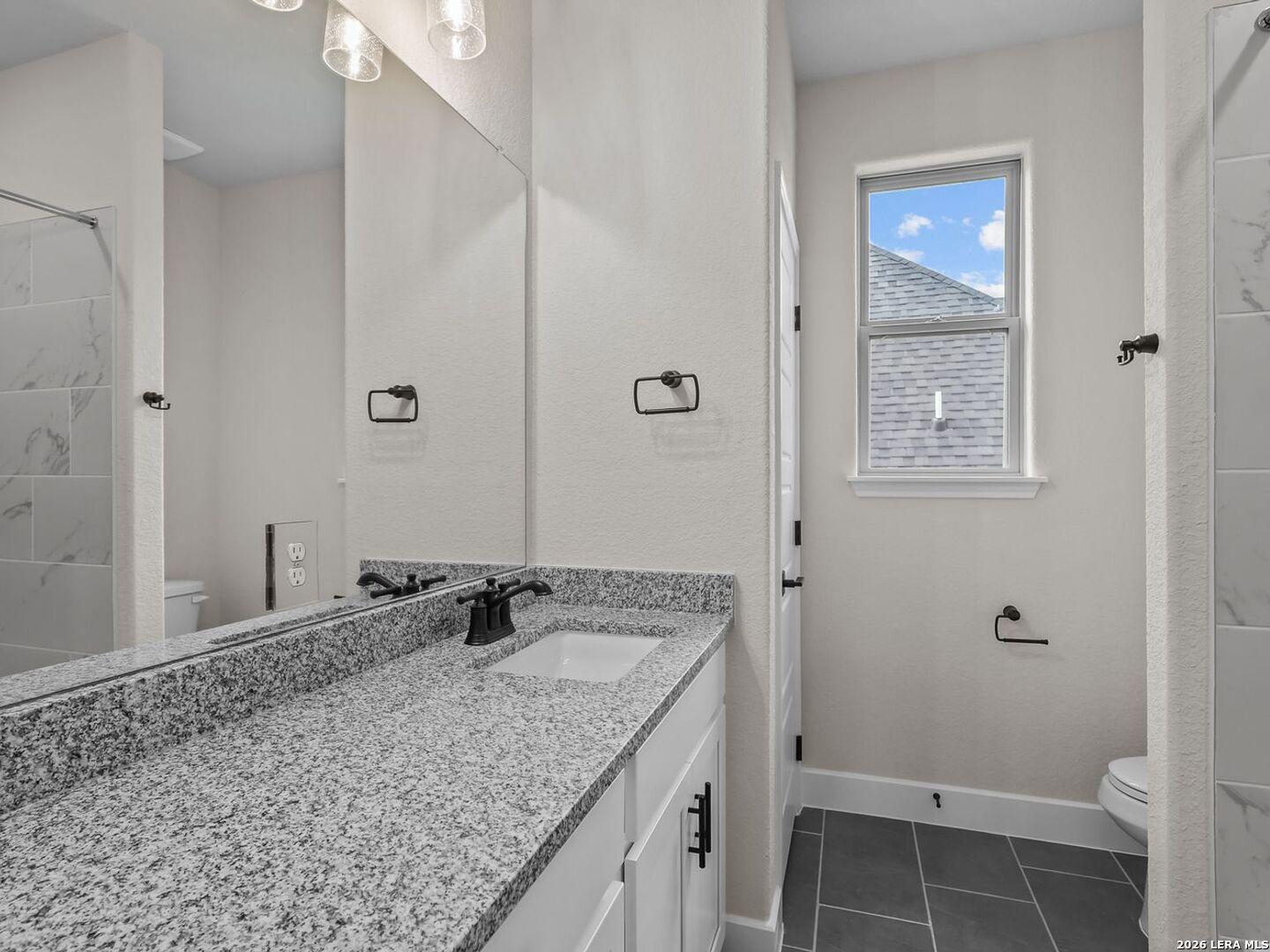 Modern bathroom with granite vanity, dark fixtures, and tiled walk-in shower in a Davidson Homes Belmont H in Castroville.