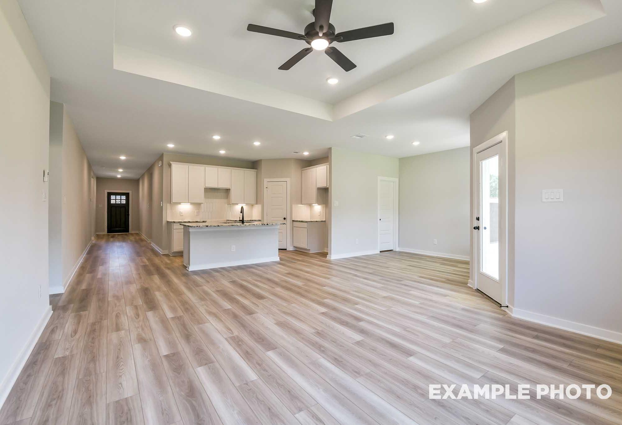 Spacious open-concept kitchen and living area in The Daphne F with white cabinets, large island, hardwood floors, and ceiling fans
