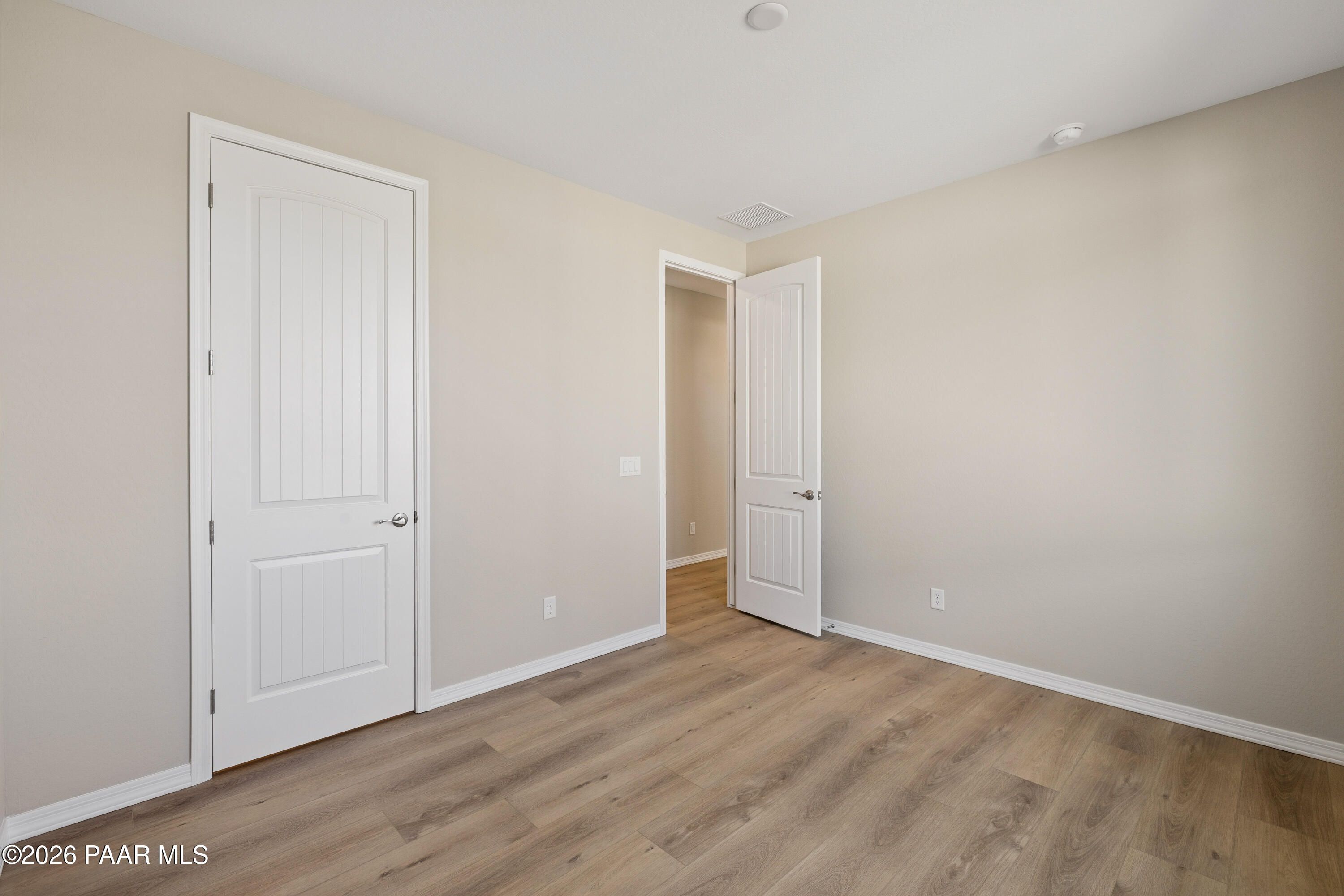 Bright secondary bedroom with beige walls, white paneled doors, and light wood flooring in Davidson Homes The Harmony A, Prescott Valley