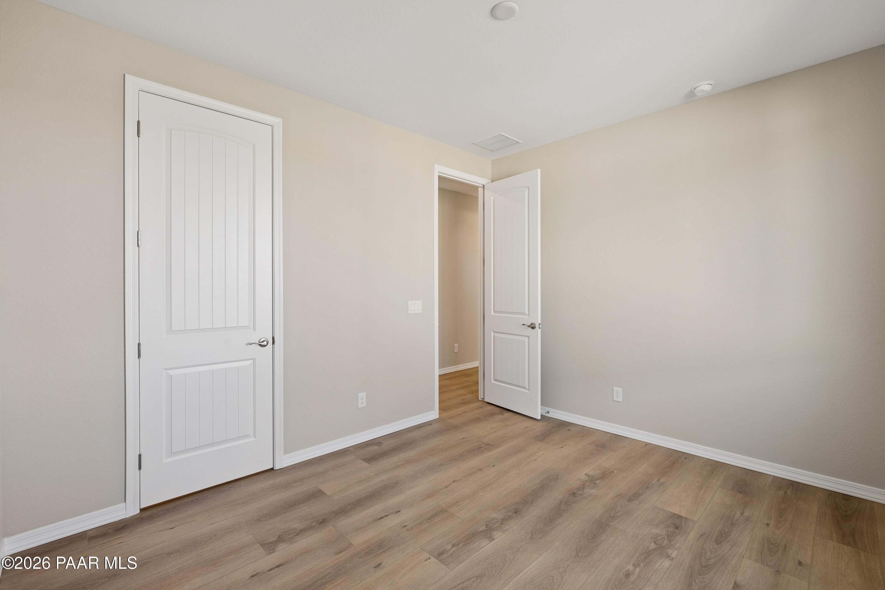 Bright secondary bedroom with beige walls, white paneled doors, and light wood flooring in Davidson Homes The Harmony A, Prescott Valley