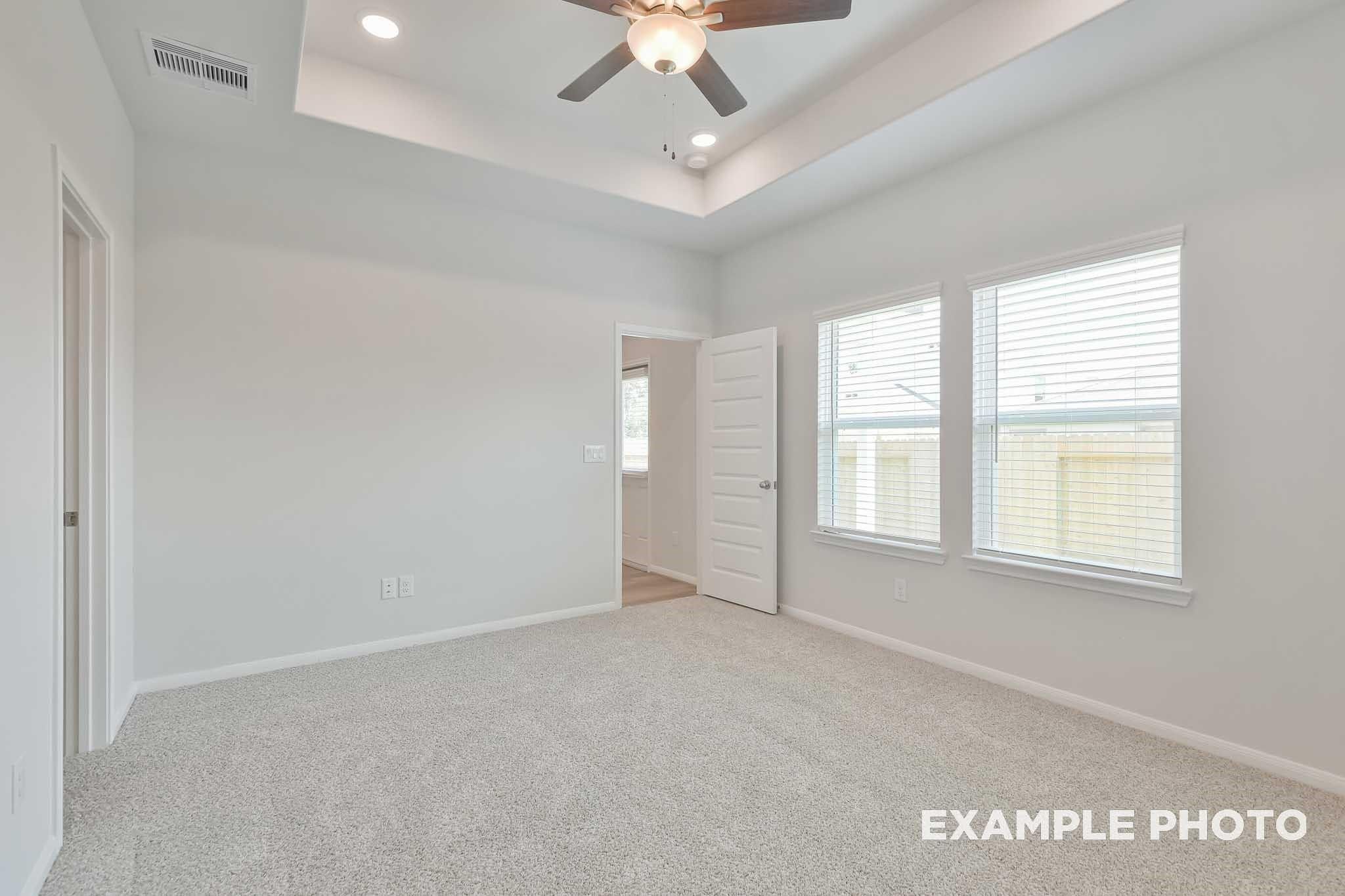 Spacious bedroom with tray ceiling, ceiling fan, recessed lights, and large windows in Davidson Homes The Frio F, Conroe, Texas