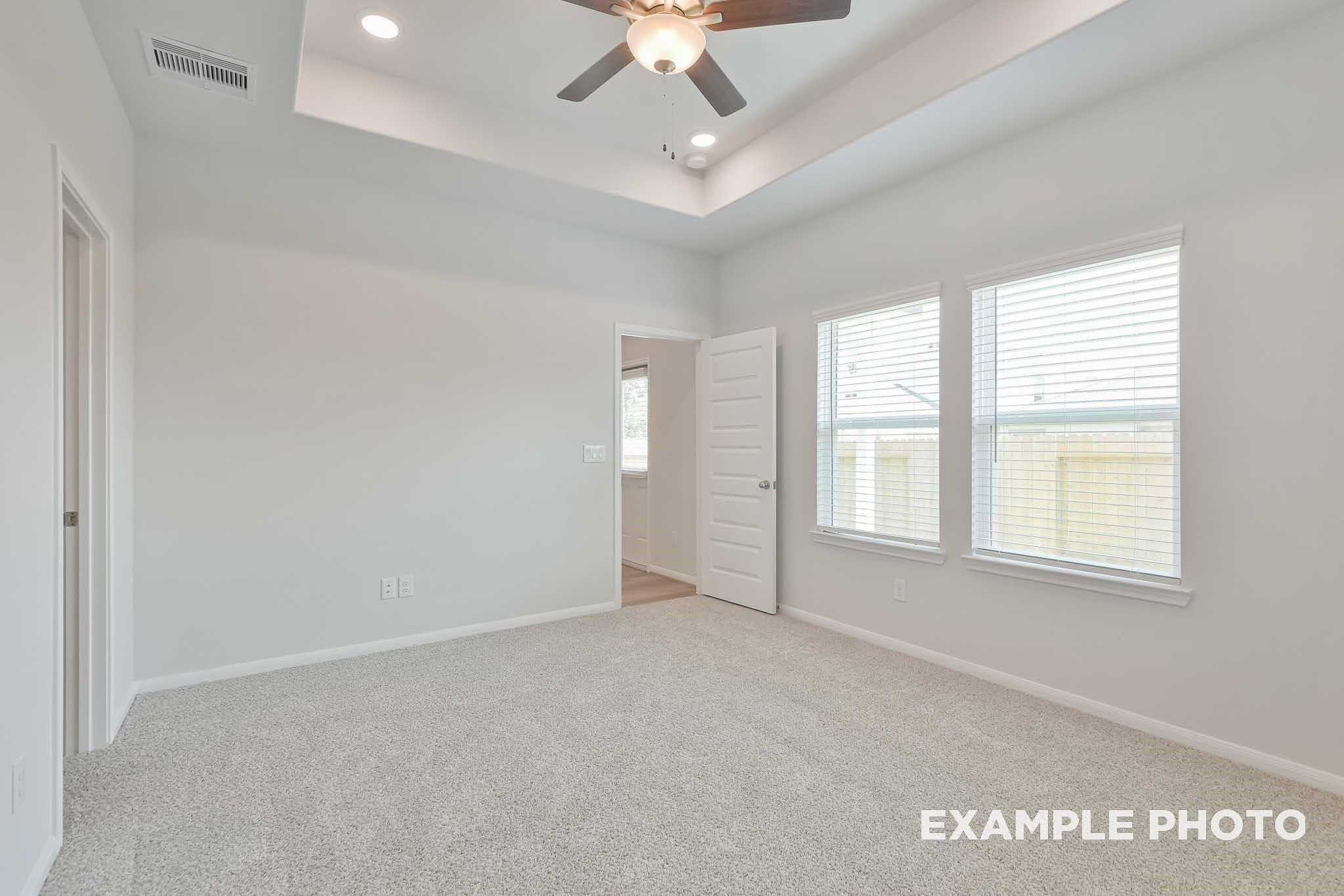 Spacious bedroom with tray ceiling, ceiling fan, recessed lights, and large windows in Davidson Homes The Frio F, Conroe, Texas