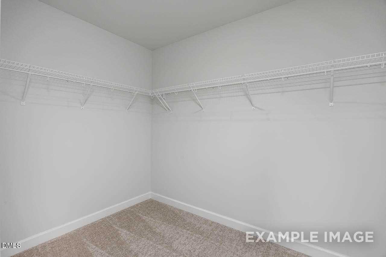 Spacious walk-in closet featuring white wire shelving and beige carpet in Davidson Homes The Graham Exterior, Fuquay-Varina, NC