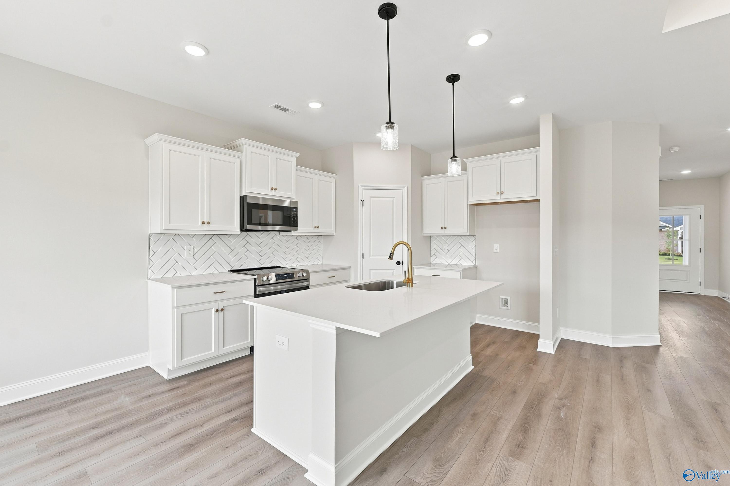 Modern kitchen with white cabinets, quartz island, and herringbone backsplash in The Asheville E home, Forest Glen, Alabama.