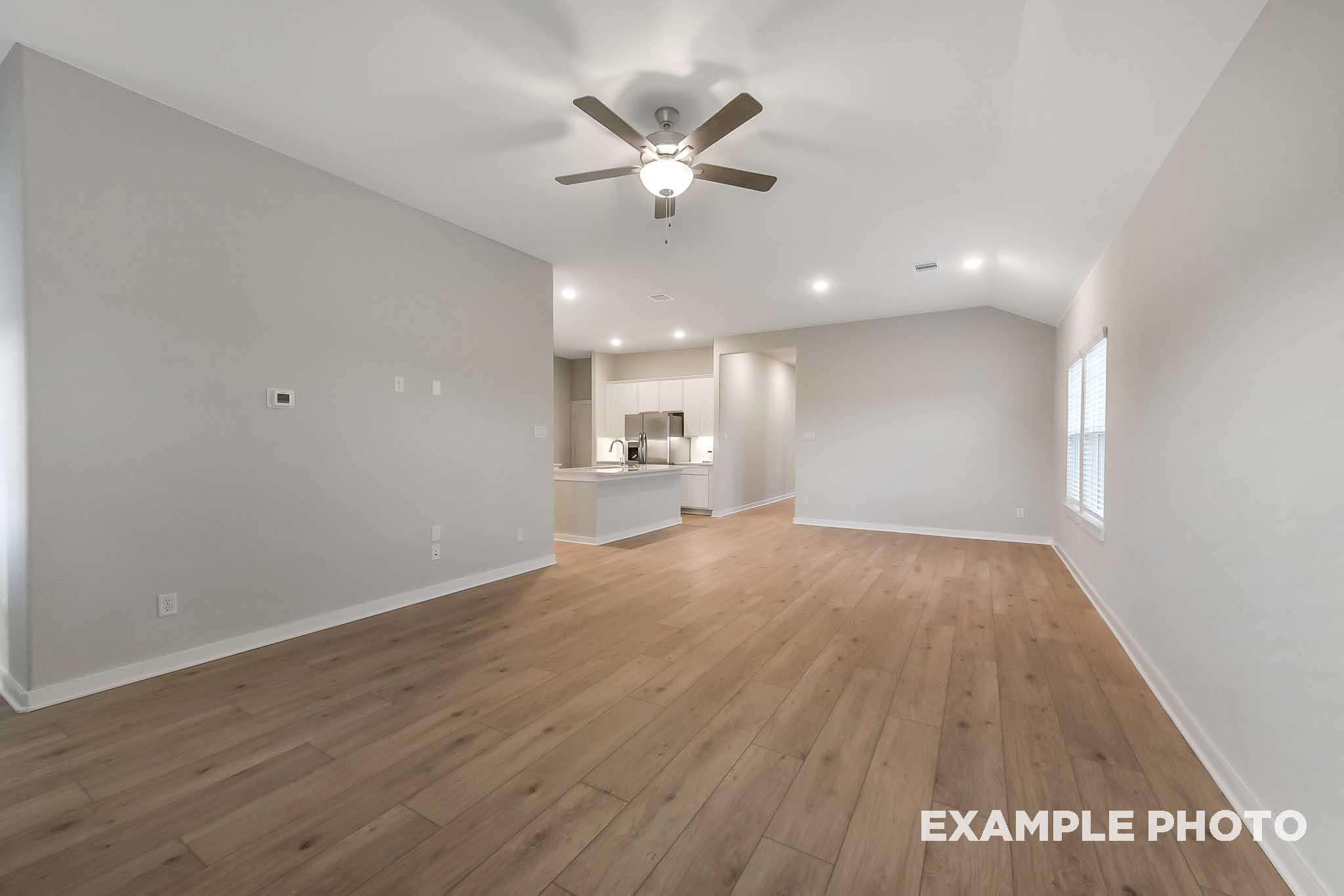 Spacious open-concept living room in The Laguna B with hardwood floors, ceiling fan, neutral walls, and kitchen overlook