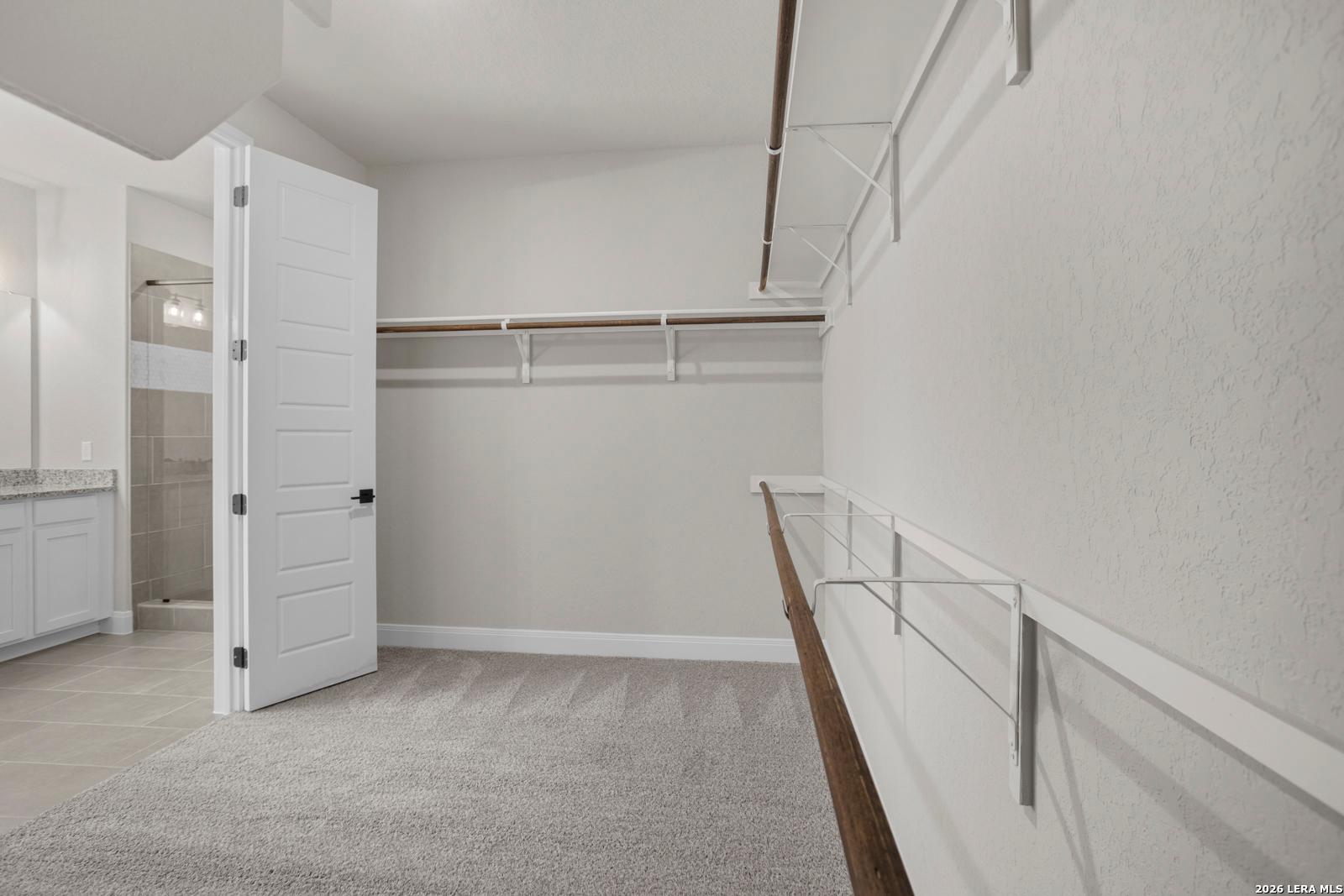 Walk-in closet with carpeted floors and shelving in The Jennings G floor plan by Davidson Homes in Ladera, San Antonio.