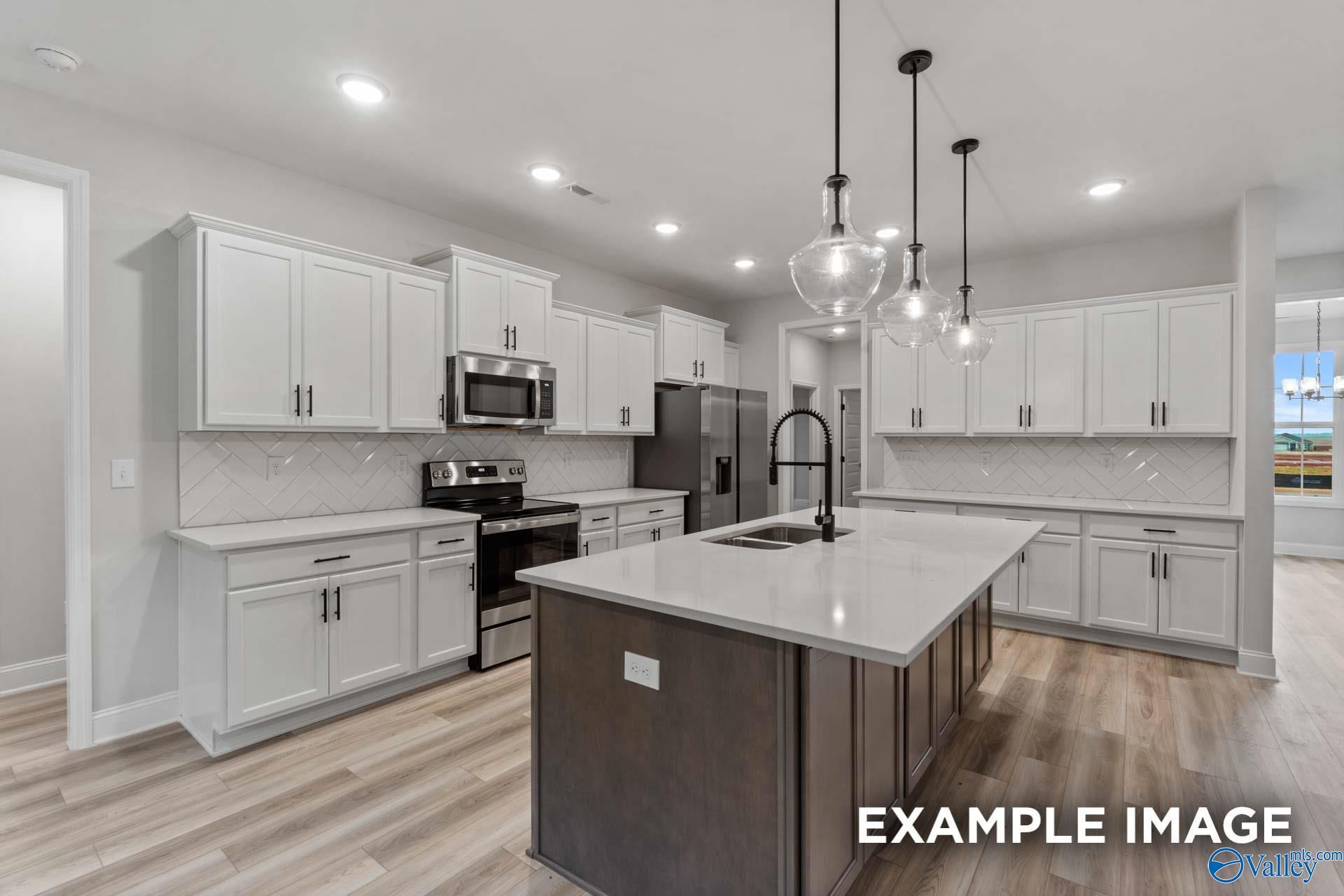 Modern open-concept kitchen with white shaker cabinets, stainless appliances, quartz island, subway tile backsplash in Davidson Homes The Finleigh, Meridianville, Alabama