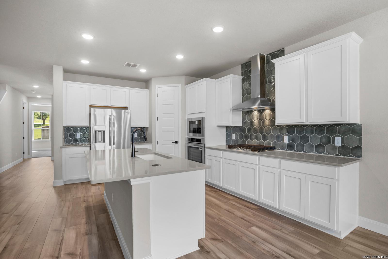 Modern kitchen with white cabinets, quartz island, and hexagon tile backsplash in The Jennings G plan, Ladera, San Antonio.