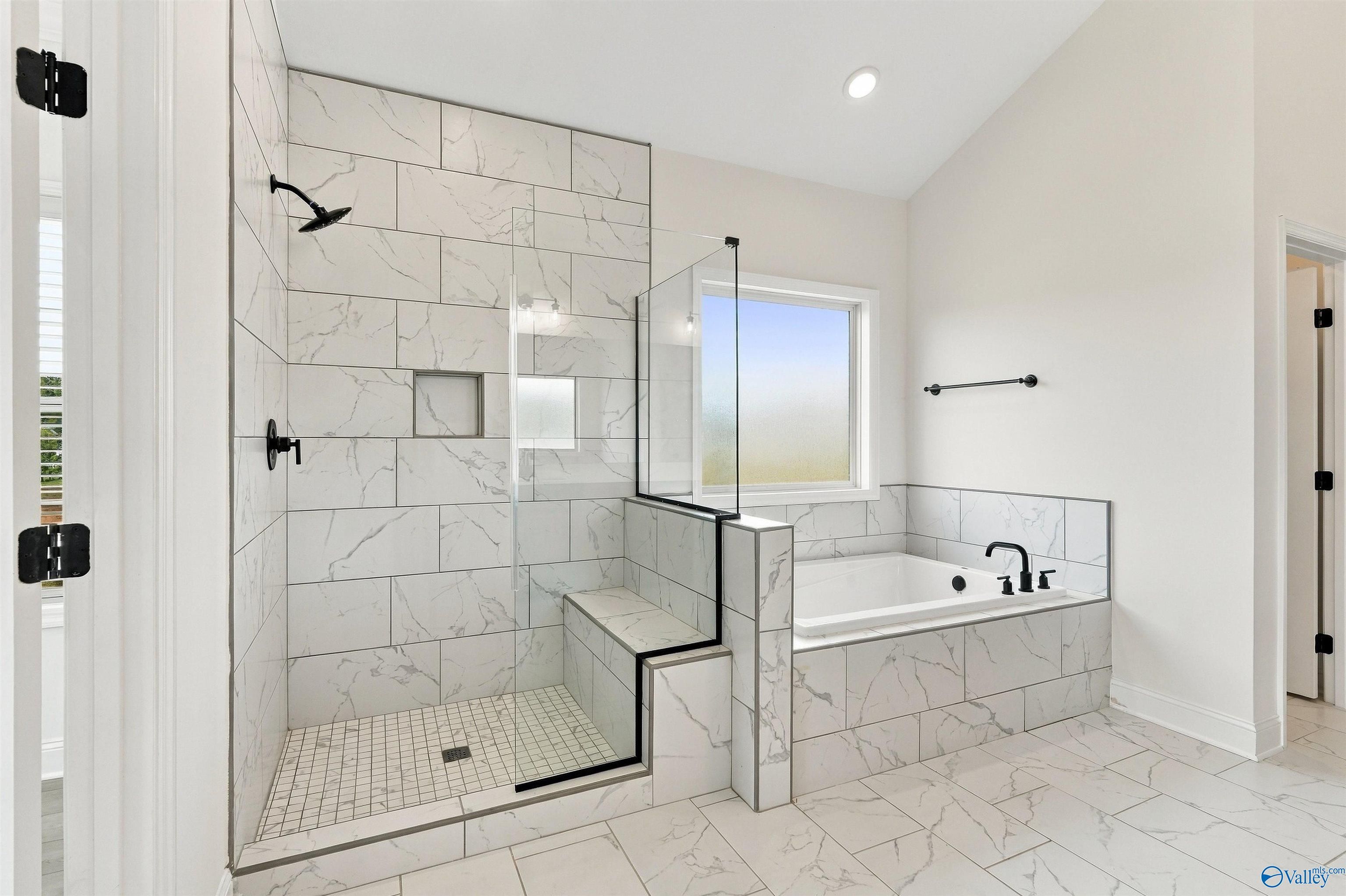 Elegant primary bathroom with marble tile walk-in shower, garden tub, and black fixtures in Davidson Homes' Valencia plan, Huntsville, AL