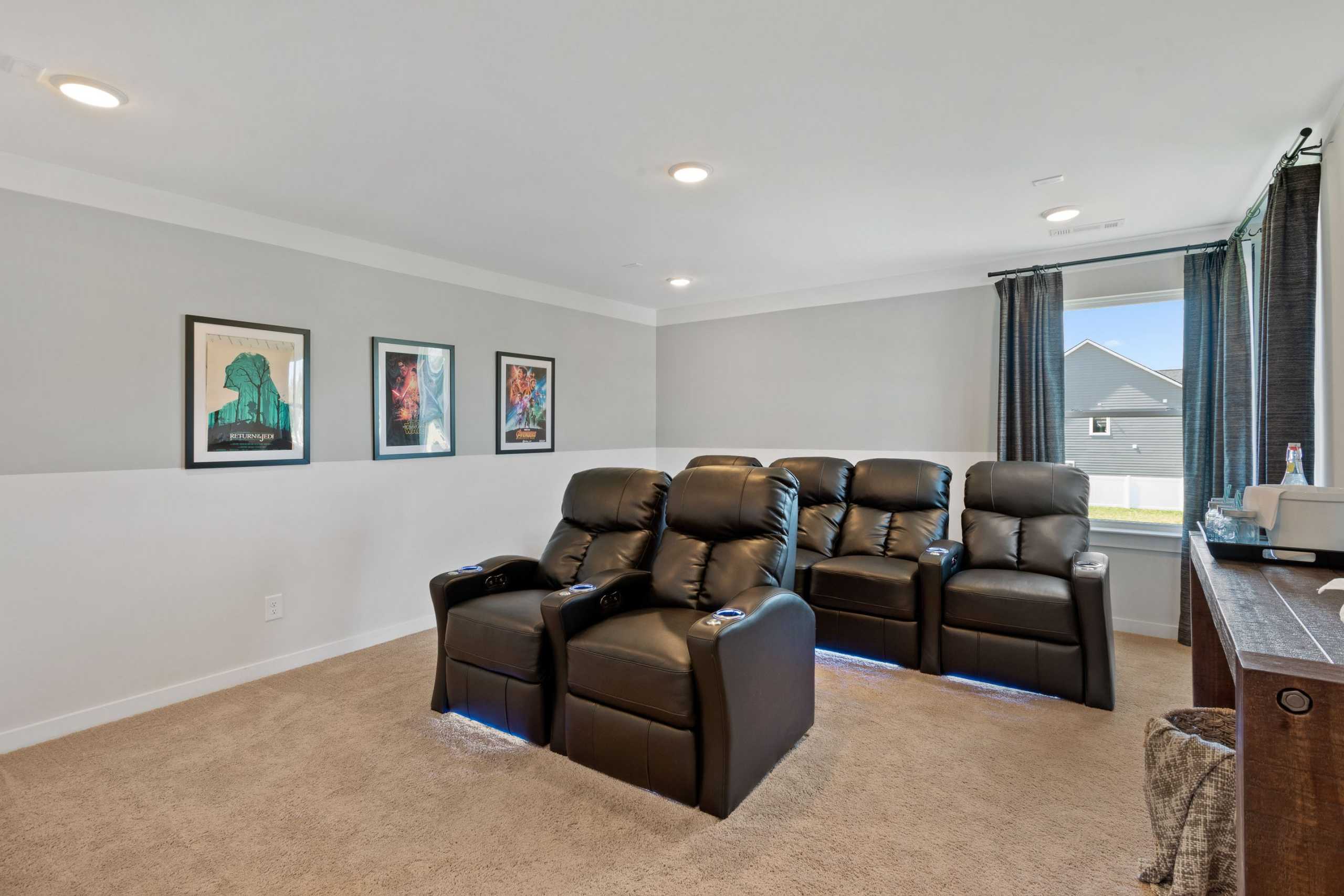 Home theater room at Rivers Edge in Murfreesboro TN with black leather recliners, movie posters, and carpeted floor