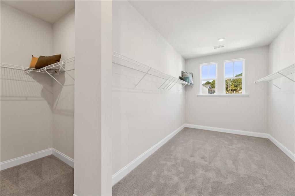 Spacious walk-in closet with wire shelving, beige walls, carpeted floor and large windows in Davidson Homes The Danbury C, Buford, GA