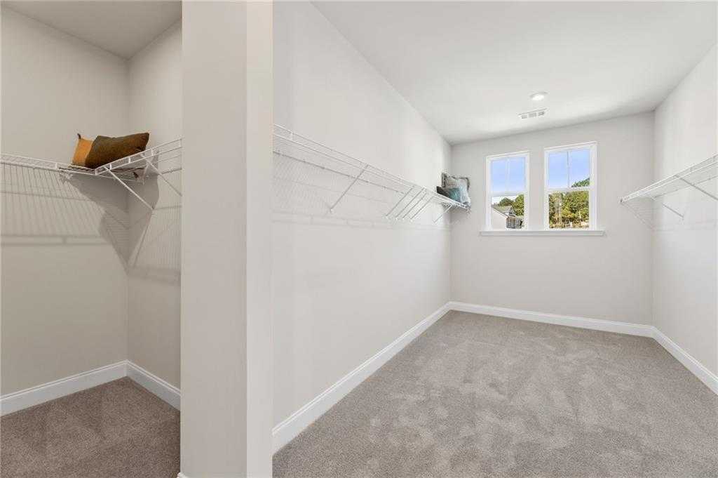 Spacious walk-in closet with wire shelving, beige walls, carpeted floor and large windows in Davidson Homes The Danbury C, Buford, GA