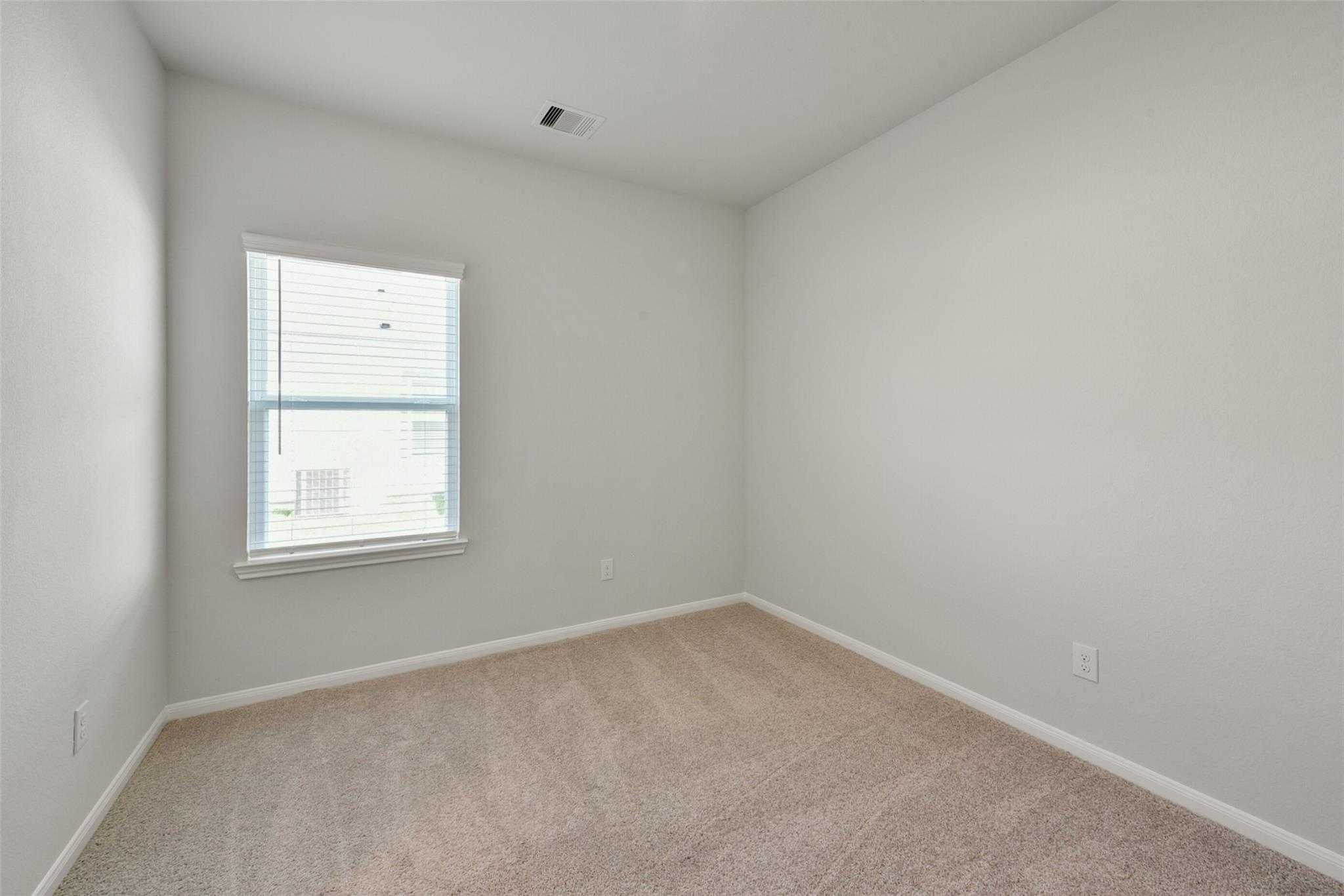 Bright empty bedroom with neutral gray walls, beige carpet floor, and large window in Davidson Homes Sabine E, Dayton, Texas