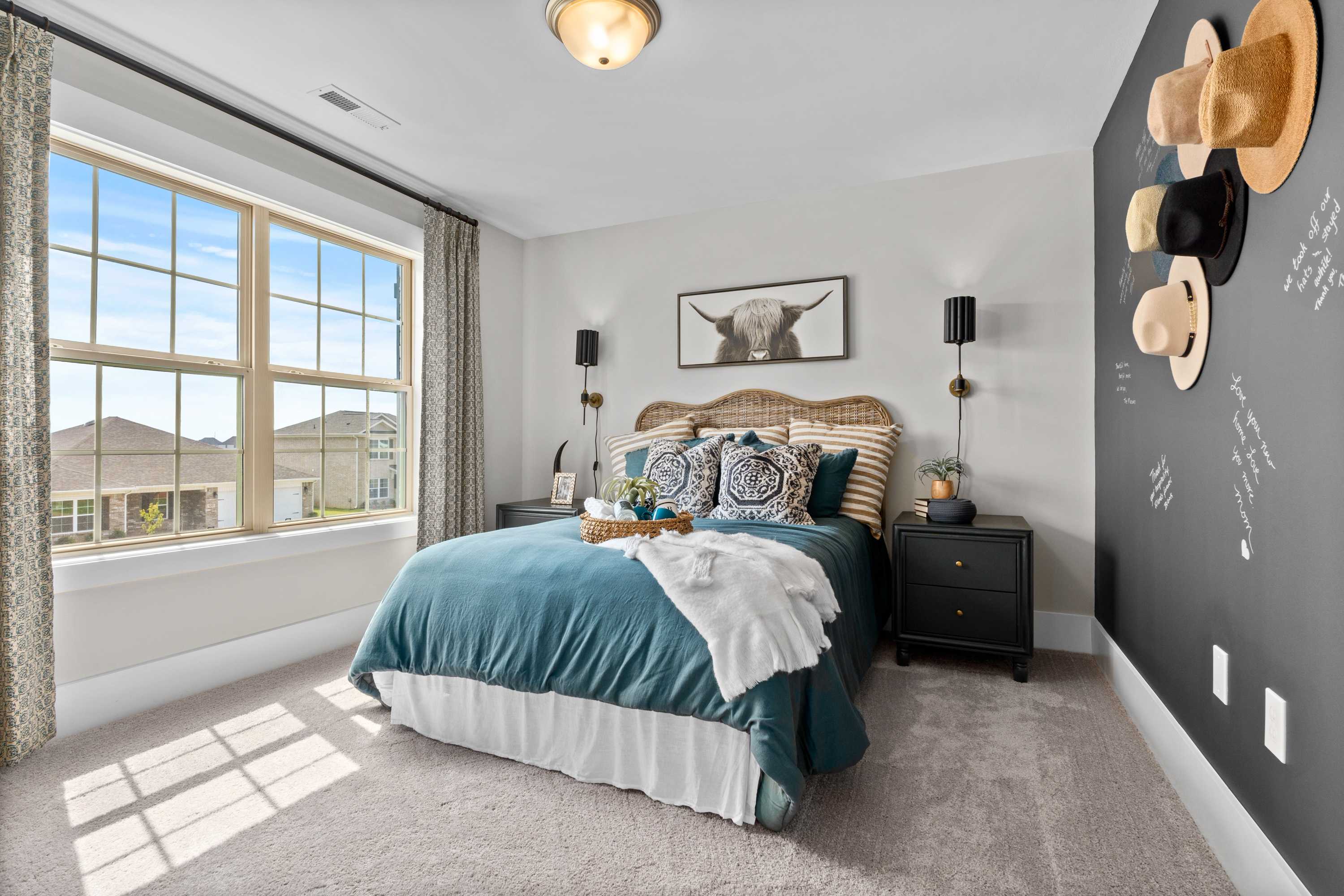 Upper floor master bedroom in The Chelsea B featuring teal bedding, hat wall decor, blackboard accent, and large windows