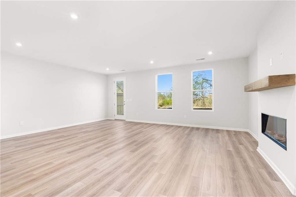 Spacious living room with modern linear gas fireplace, large windows, French doors, and light wood floors in Davidson Homes The Cary A, Winder GA