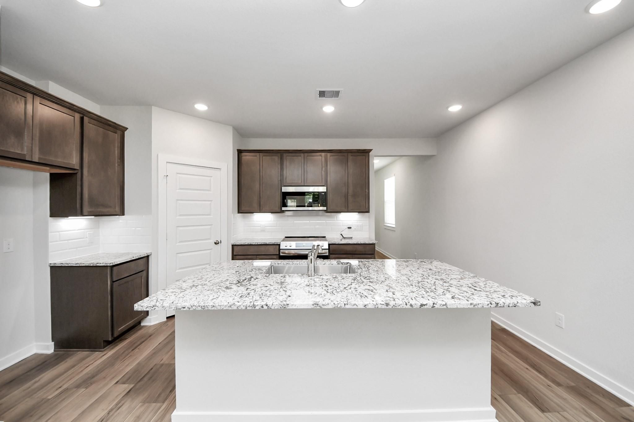 Modern kitchen with granite island, dark cabinets, and stainless appliances in The Sabine E home at Liberty Estates, TX.