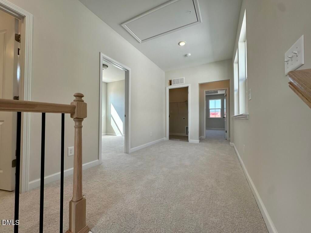 Bright upstairs hallway with oak staircase, black railings, beige carpet, and doorways in Davidson Homes The Burke, Knightdale, NC