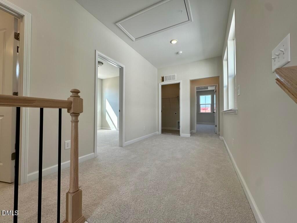 Bright upstairs hallway with oak staircase, black railings, beige carpet, and doorways in Davidson Homes The Burke, Knightdale, NC