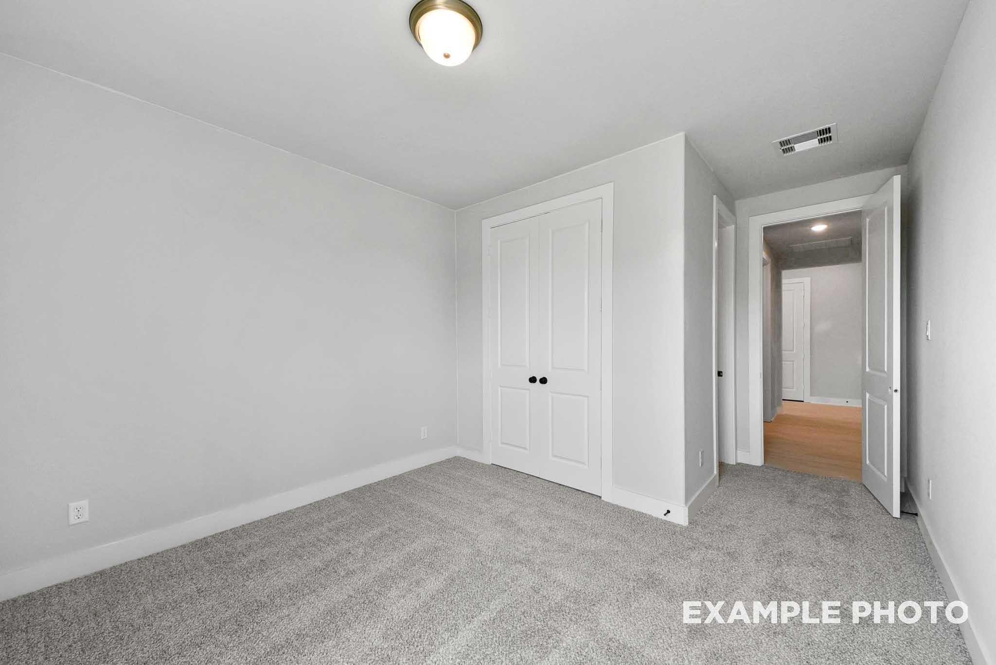 Empty secondary bedroom featuring gray carpet, white double-door closet, and open hallway access in Davidson Homes The George A, Lago Mar, Texas City