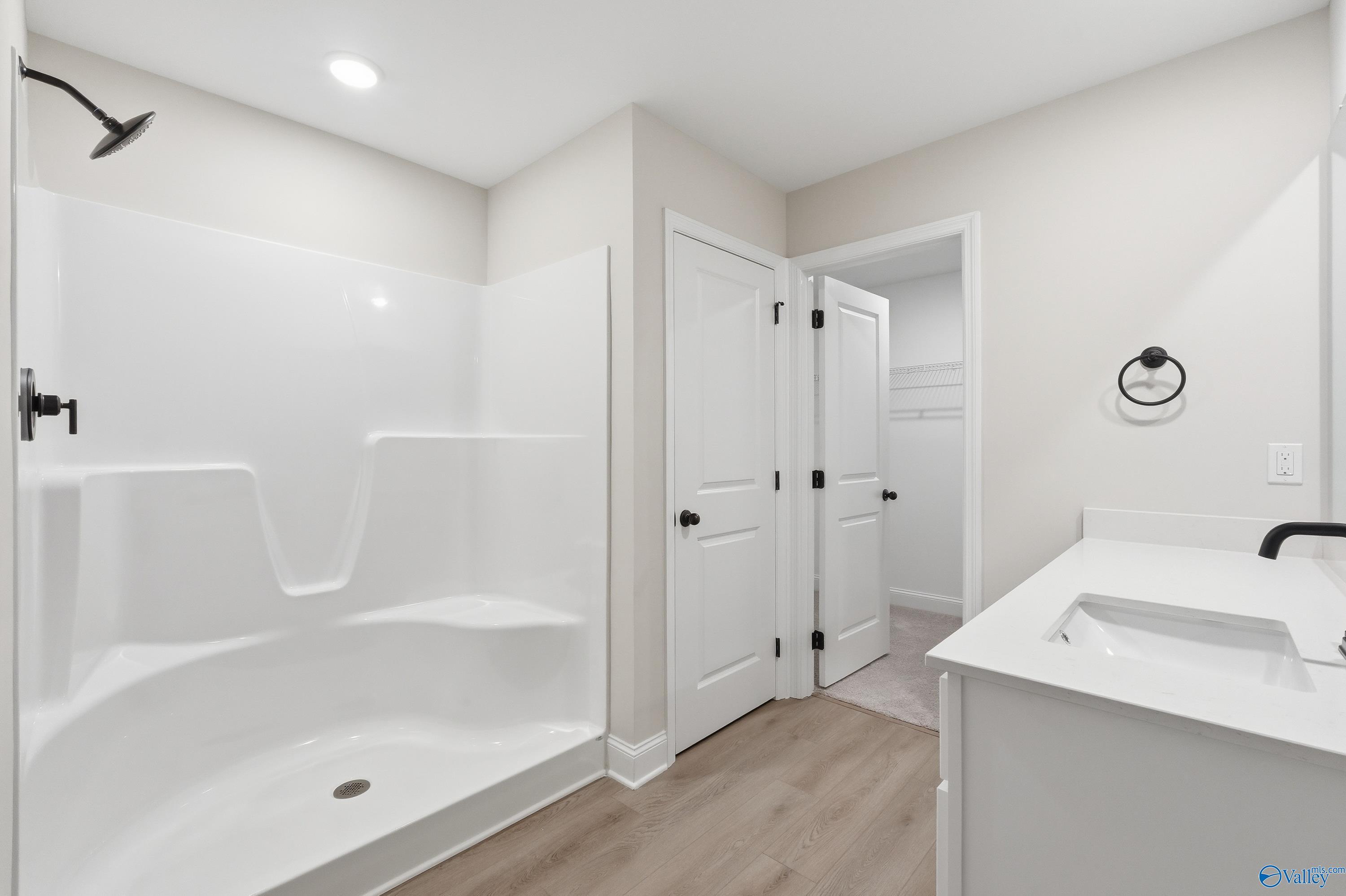 Modern master bath with white tiled walk-in shower, single vanity sink, and adjacent doors in Davidson Homes The Franklin V, Athens Alabama