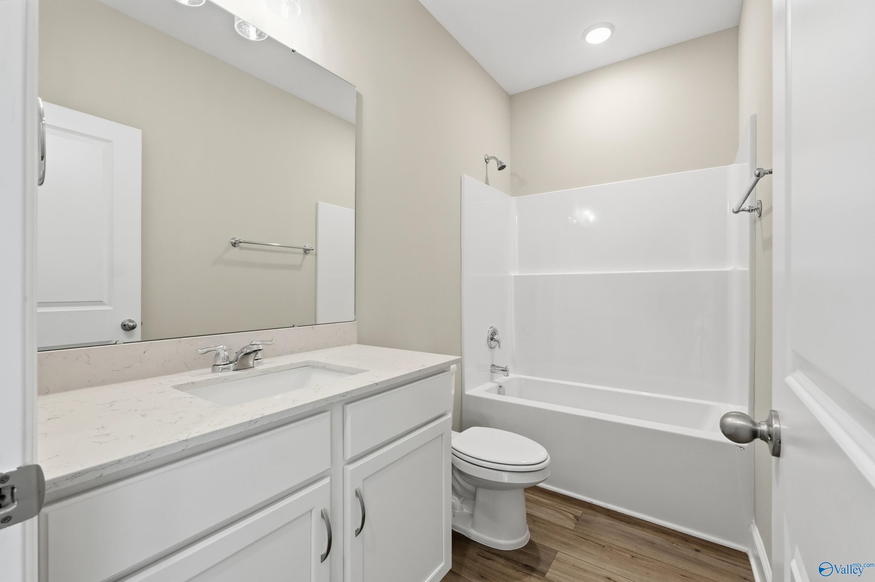 Modern bathroom with white vanity, quartz countertop, bathtub-shower combo, and wood floors in Davidson Homes The Franklin C, New Market, Alabama