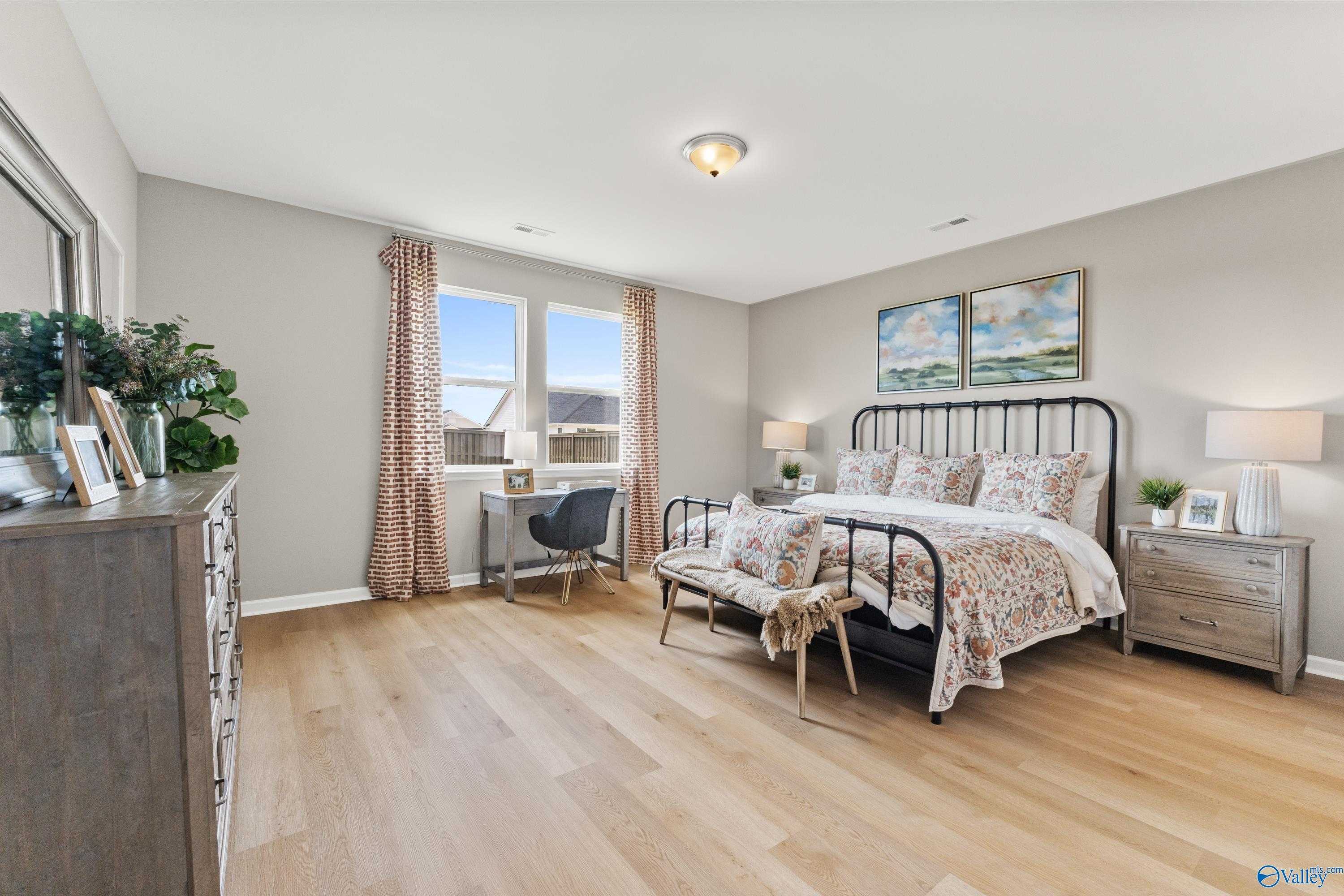 Elegant master bedroom with king bed, floral bedding, desk, and plants in Davidson Homes The Sanctuary, Athens, Alabama