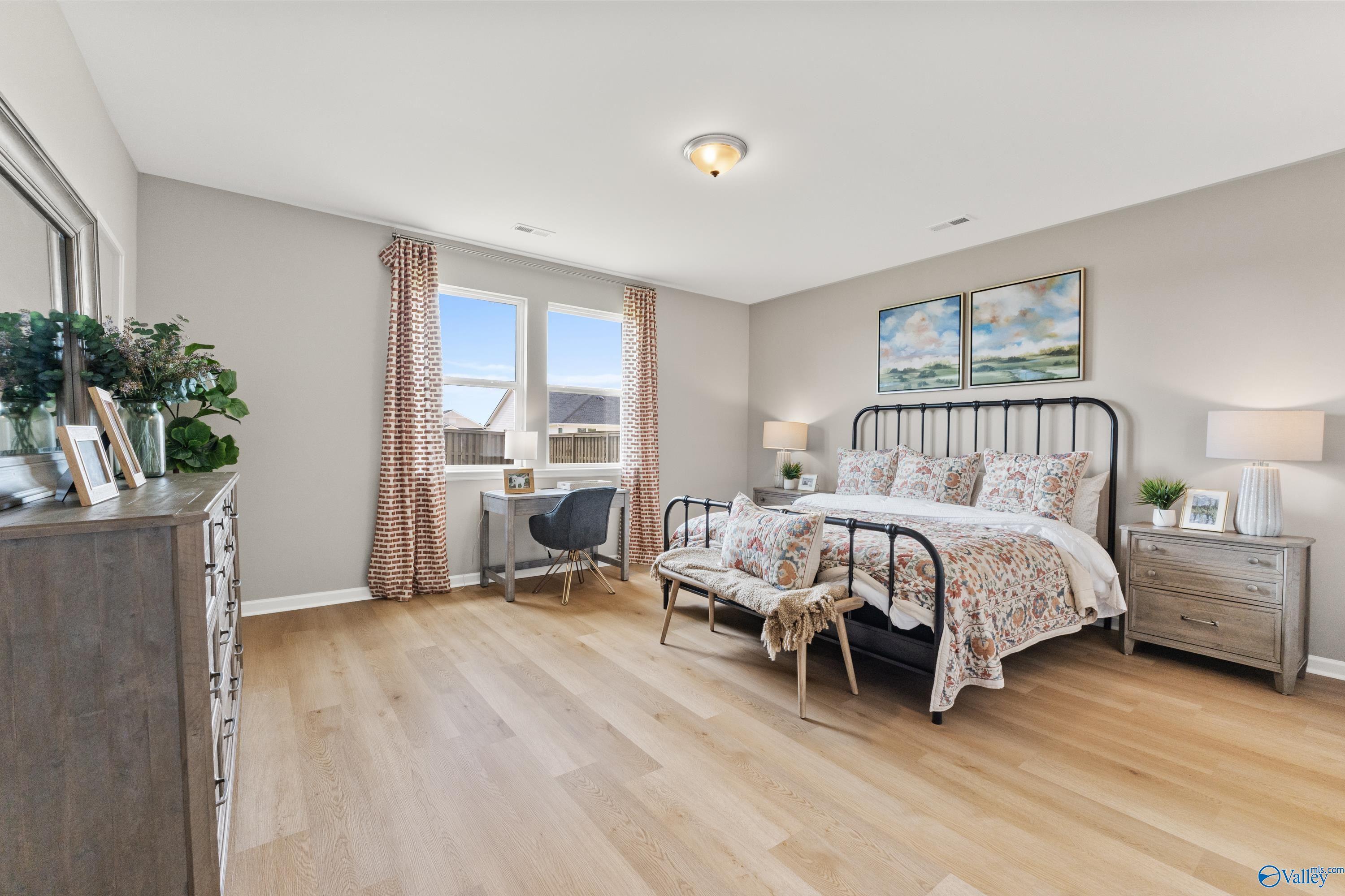 Elegant master bedroom with king bed, floral bedding, desk, and plants in Davidson Homes The Sanctuary, Athens, Alabama