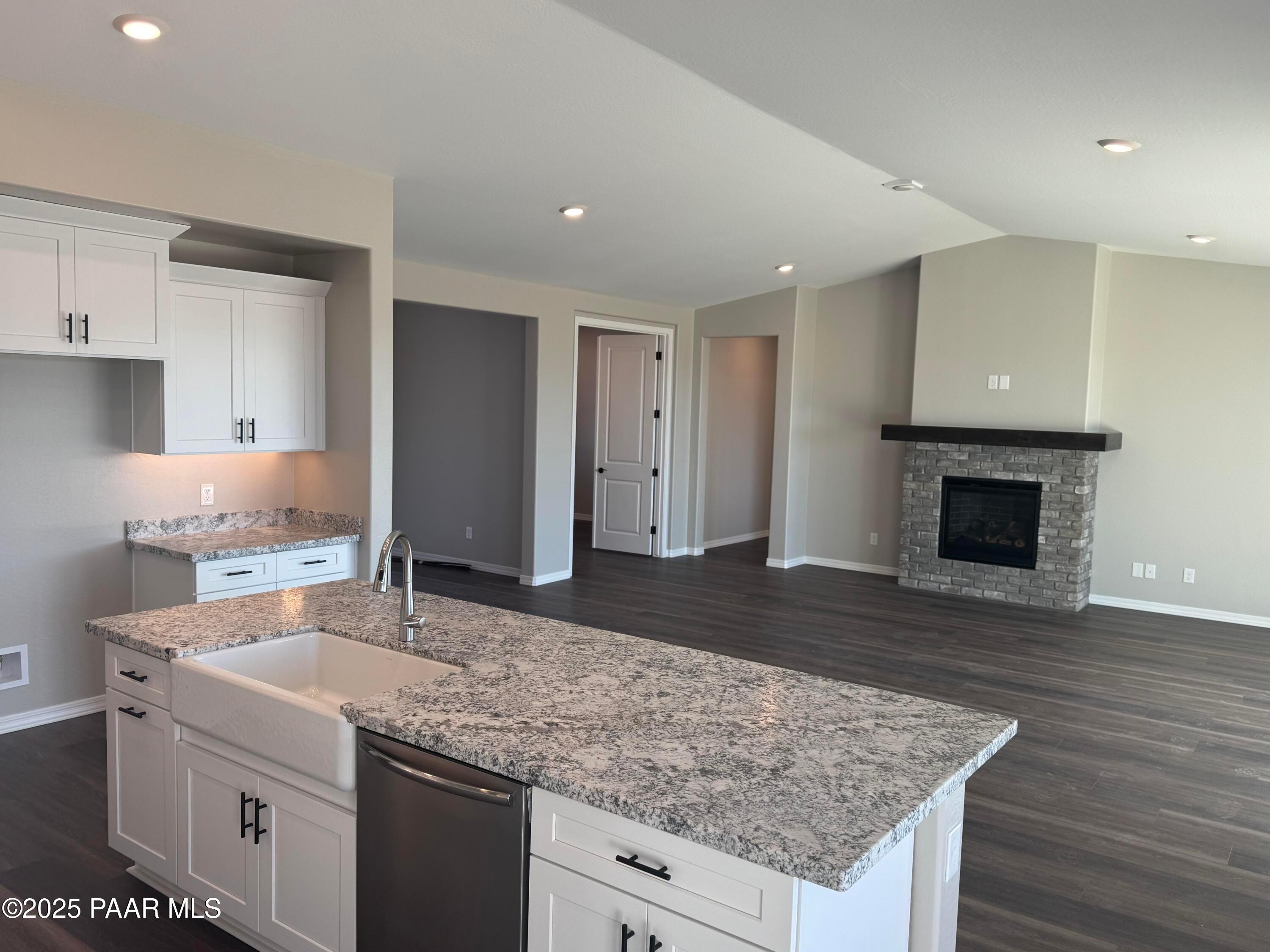 Open-concept kitchen featuring granite island, farmhouse sink, white cabinets, and stone gas fireplace in Davidson Homes The Monarch E, Prescott, AZ