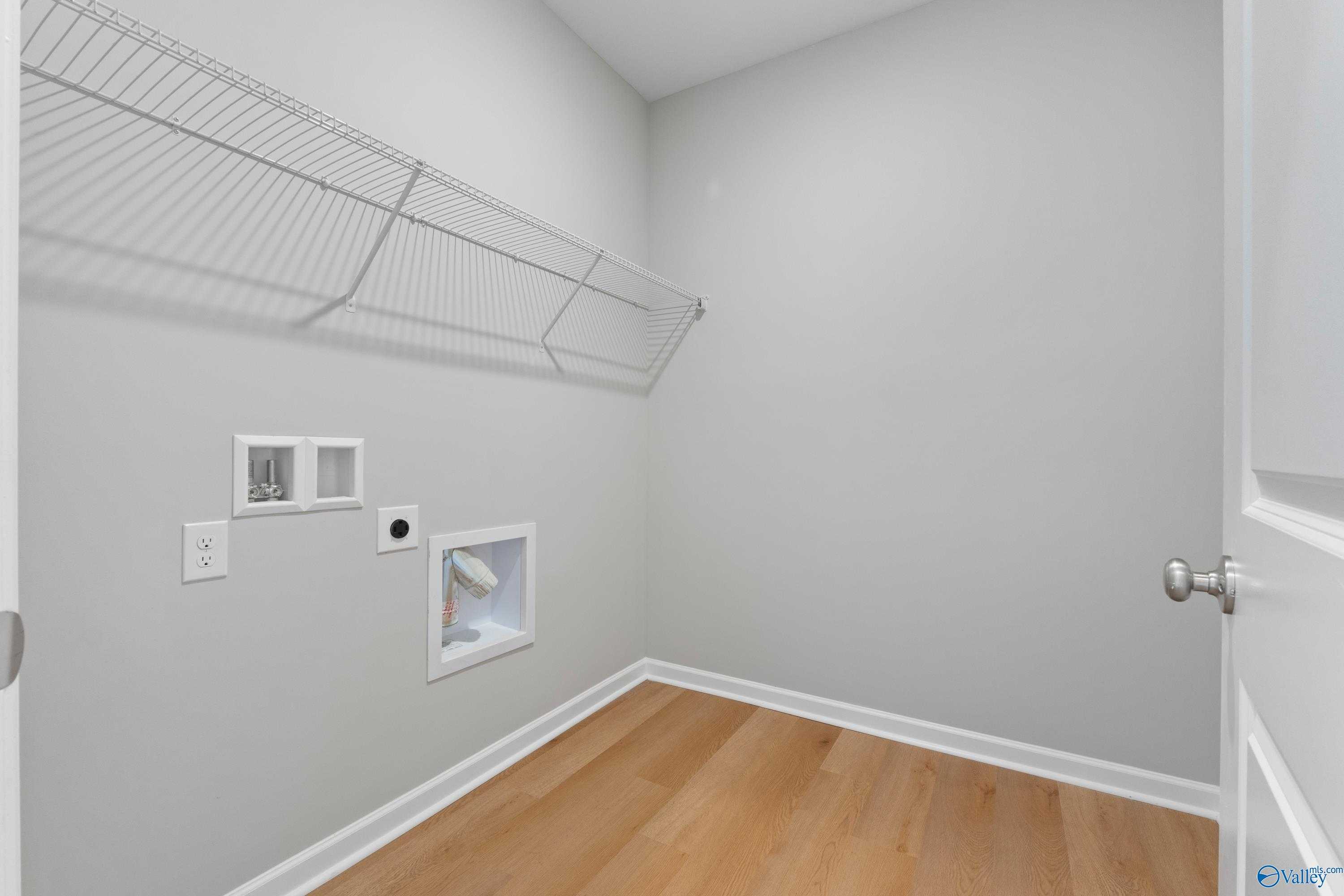 Spacious laundry room featuring wire shelving, utility sink, outlets, and hardwood floors in Davidson Homes The Orion, Athens AL