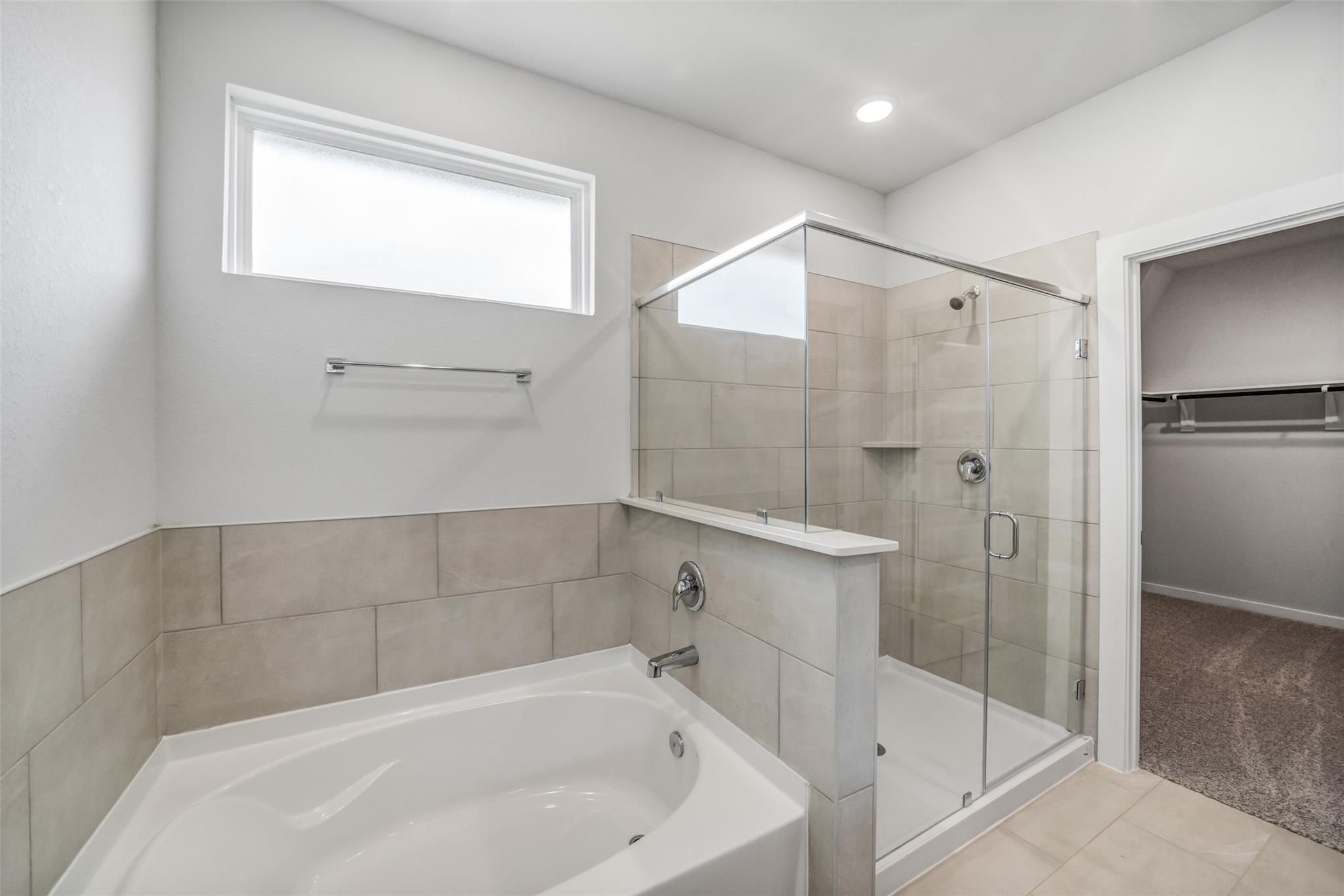 Elegant master bathroom with soaking tub, glass shower enclosure, and walk-in closet in Davidson Homes The Acadia C, Magnolia TX