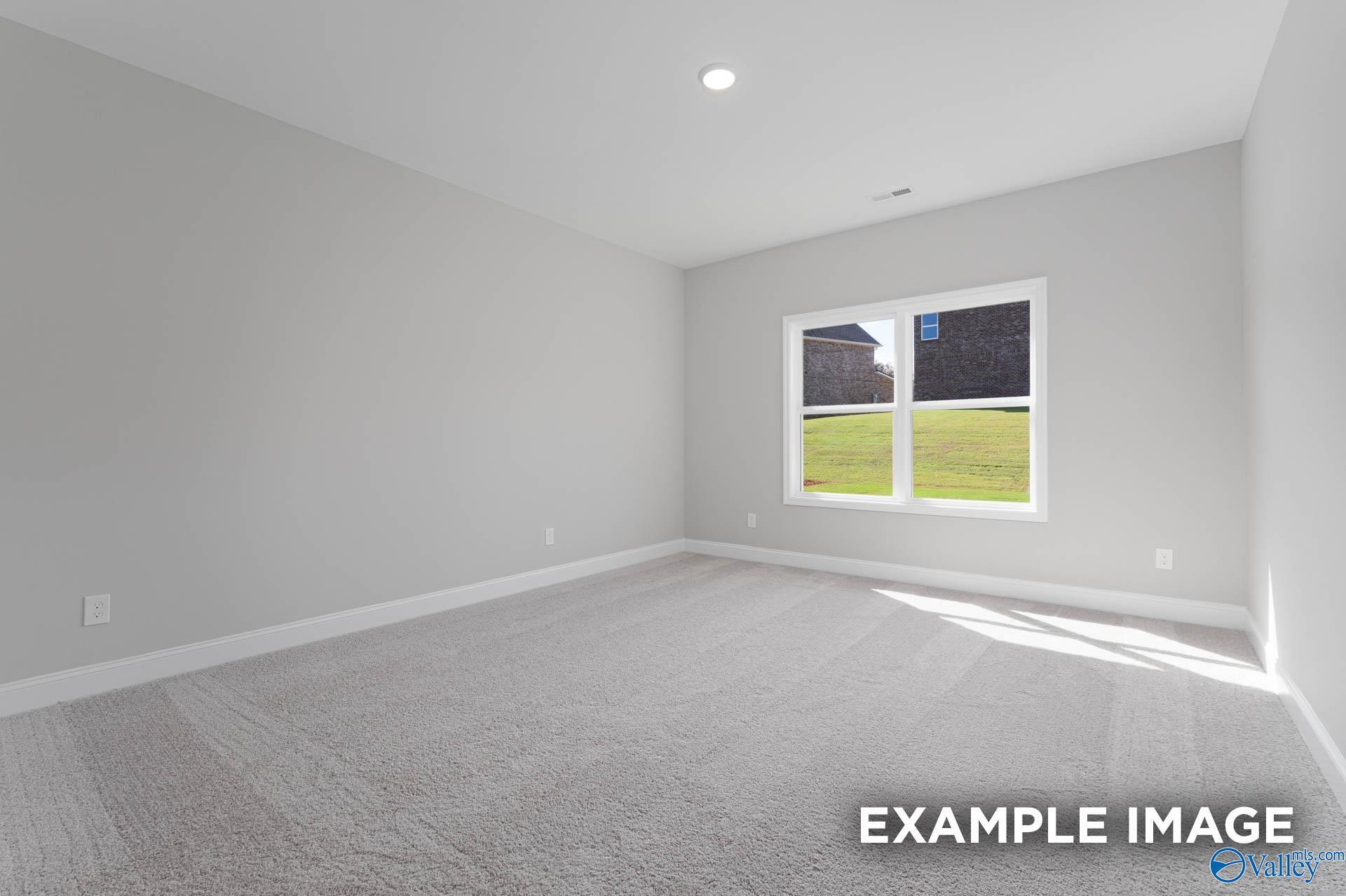 Spacious empty bedroom with light gray walls, beige carpet, and large window to green lawn in Davidson Homes The Daphne D, Meridianville, AL
