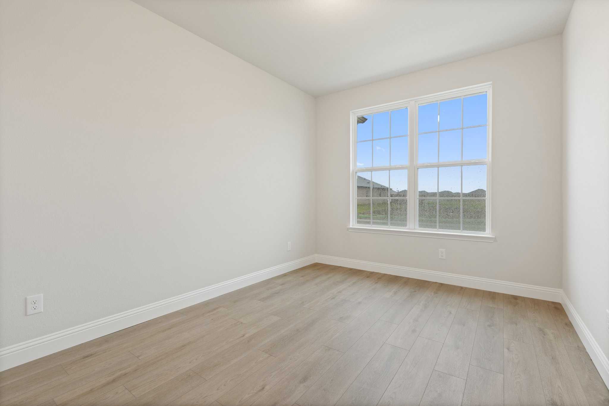 Spacious empty bedroom in The Harrison C with beige walls, light hardwood floors, and large windows overlooking scenic view