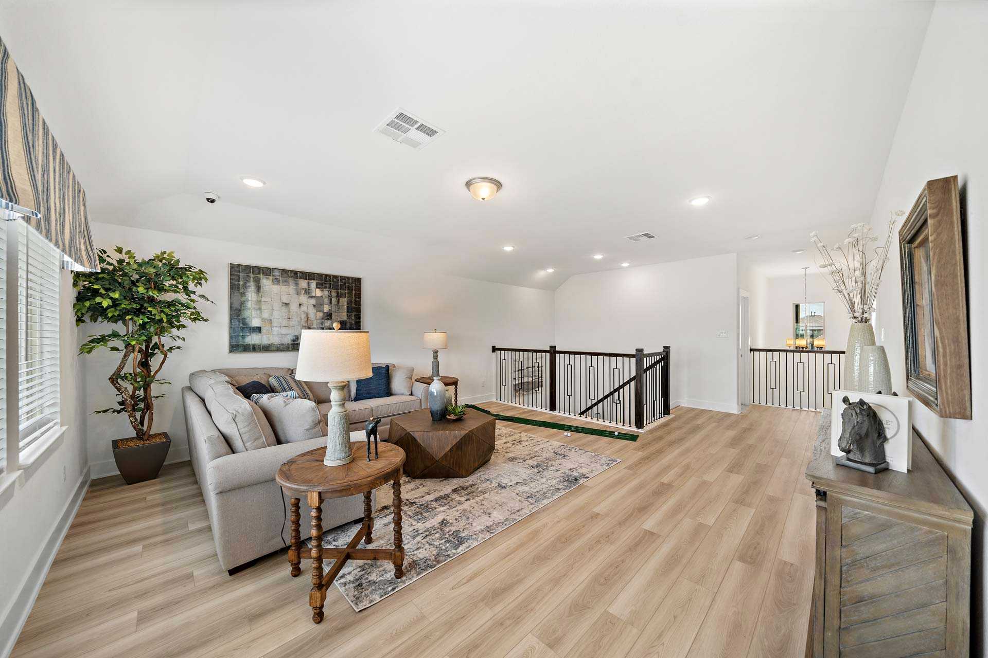 Spacious loft living area in Sierra Vista Rosharon TX by Davidson Homes with gray sofa, hardwood floors, potted plant, and staircase railing