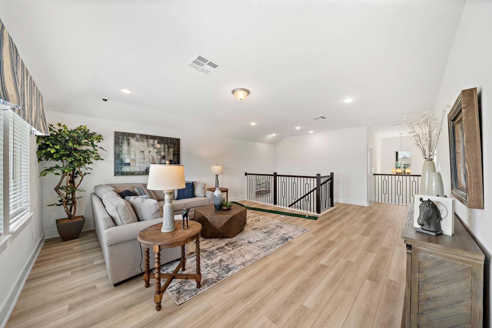 Spacious loft living area in Sierra Vista Rosharon TX by Davidson Homes with gray sofa, hardwood floors, potted plant, and staircase railing