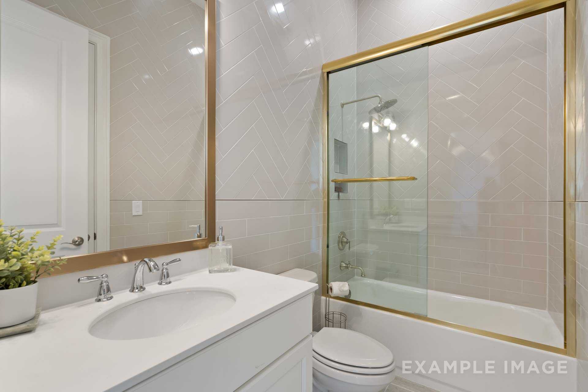 Modern master bathroom in The Seaside B with gold accents, herringbone tile walls, glass shower, and soaking tub