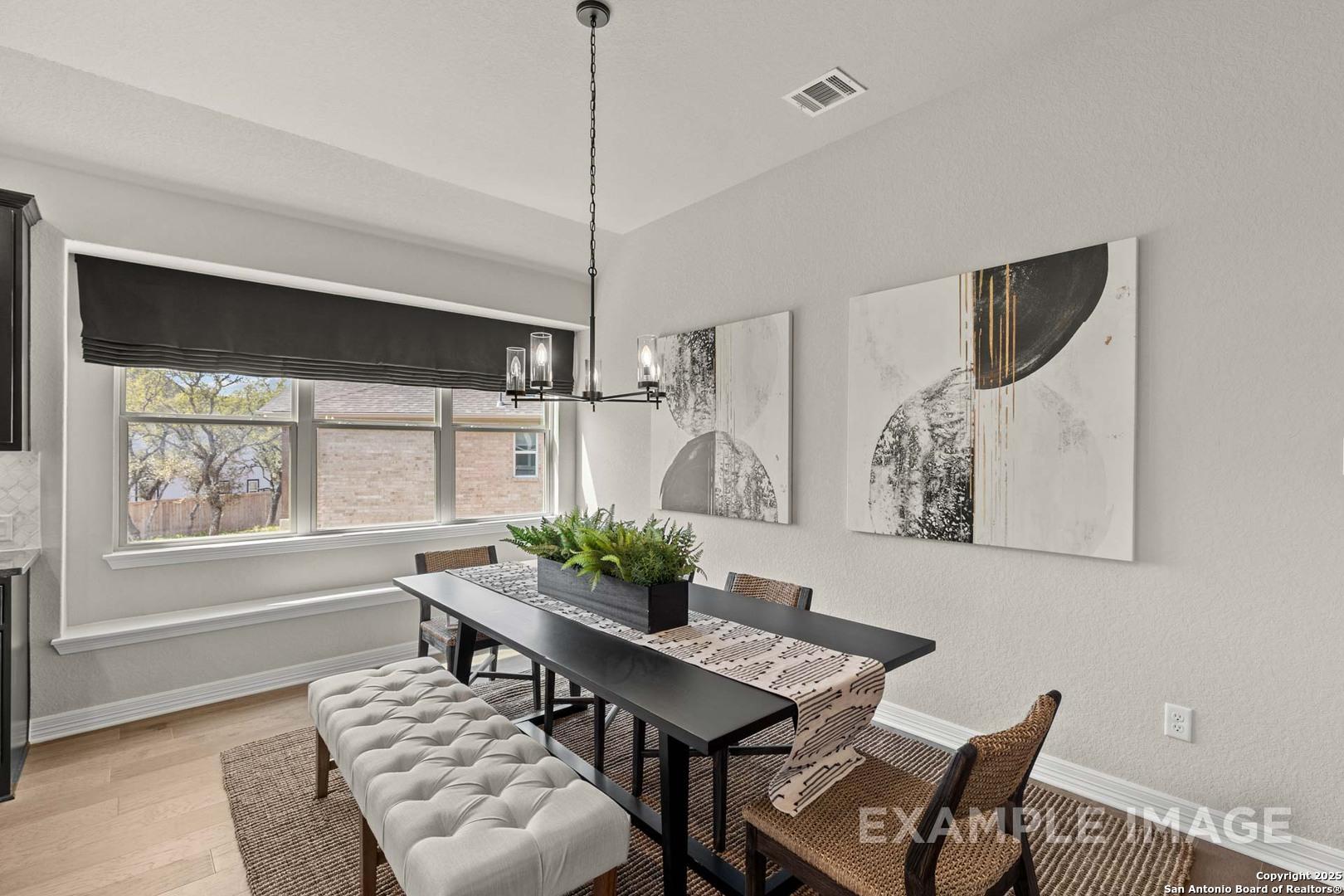 Modern dining room with large windows, chandelier, abstract art, wooden table, tufted bench, potted plant in The Summerlin B, Castroville, Texas