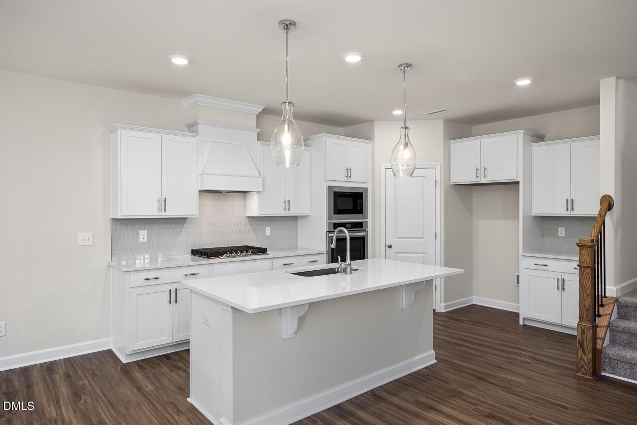 Modern white shaker kitchen with quartz island, stainless double oven, gas cooktop in Davidson Homes The Grace C, Lillington, NC