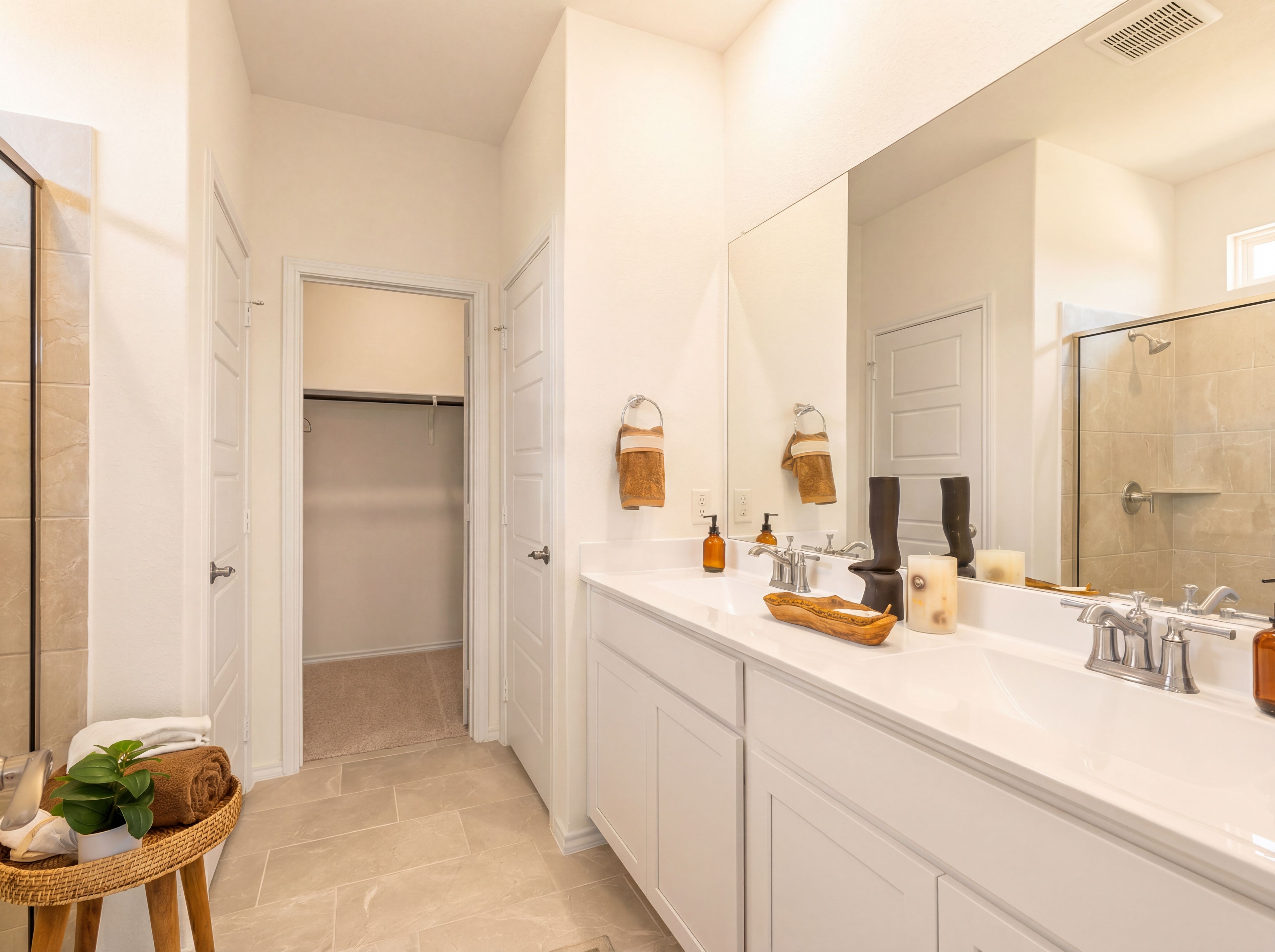 Modern primary bathroom at Rayburn Valley in San Antonio TX with double vanity, glass shower, walk-in closet, and neutral tile flooring