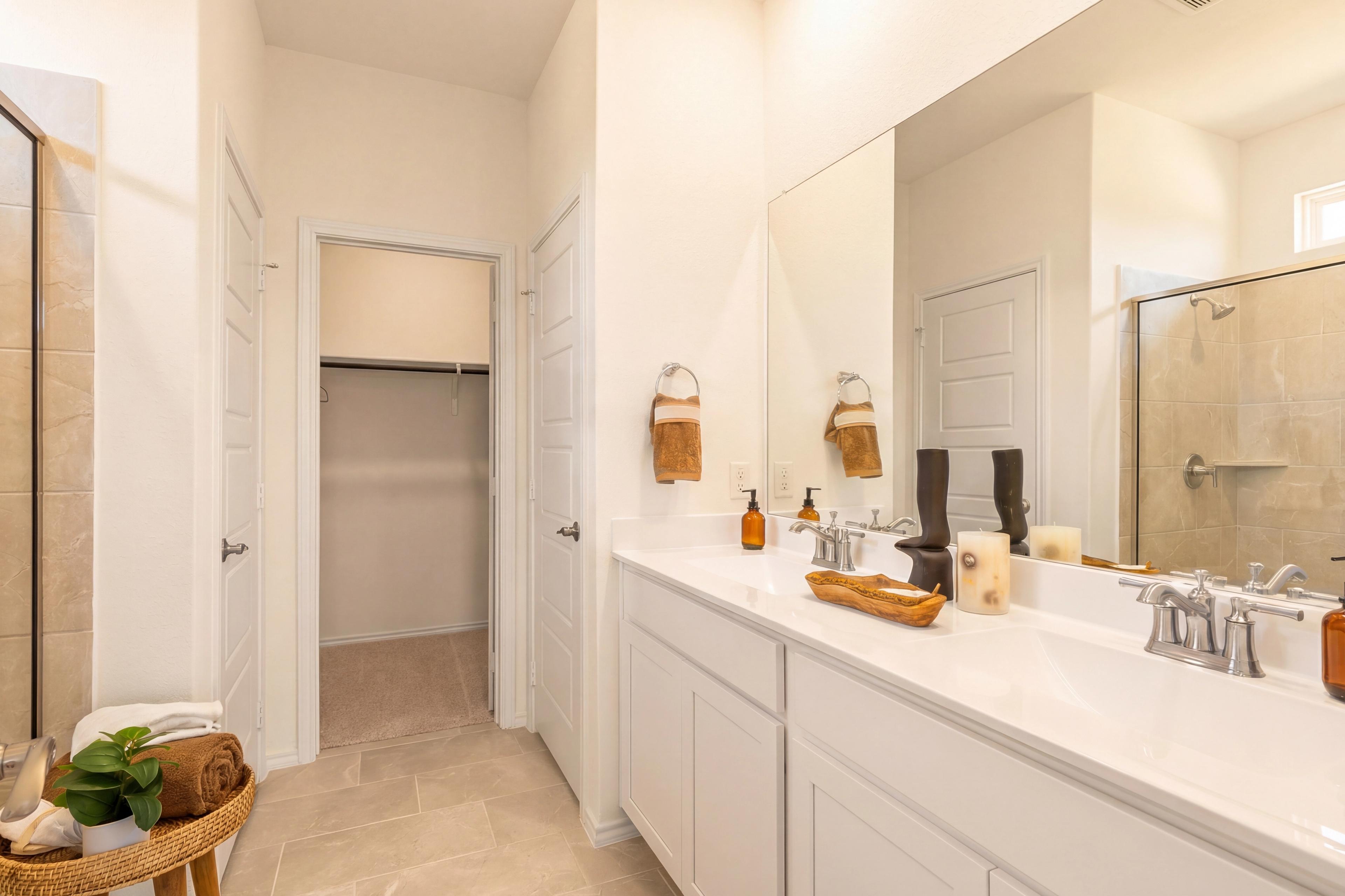 Modern primary bathroom at Rayburn Valley in San Antonio TX with double vanity, glass shower, walk-in closet, and neutral tile flooring