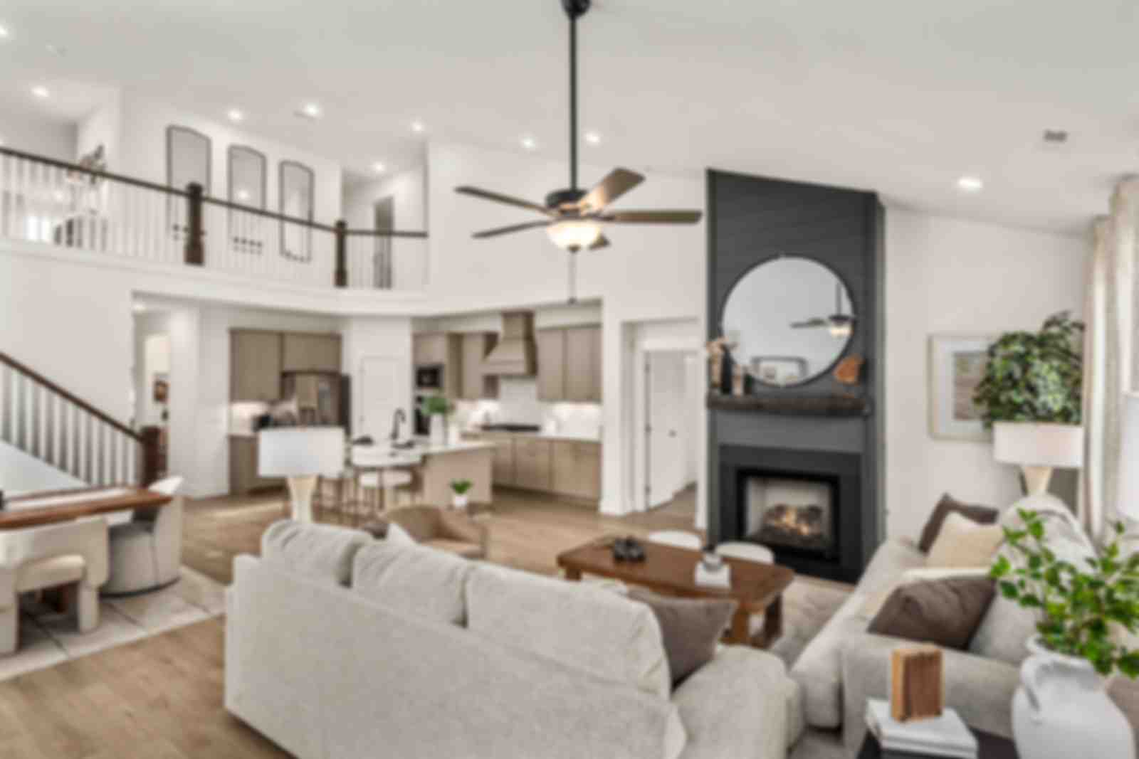 Spacious modern living room with white walls, open white kitchen, light gray sofa with green pillows, glass coffee table, har