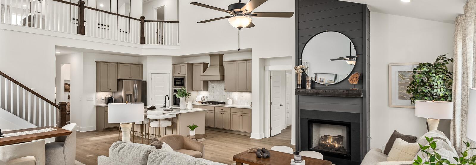 Spacious modern living room with white walls, open white kitchen, light gray sofa with green pillows, glass coffee table, har