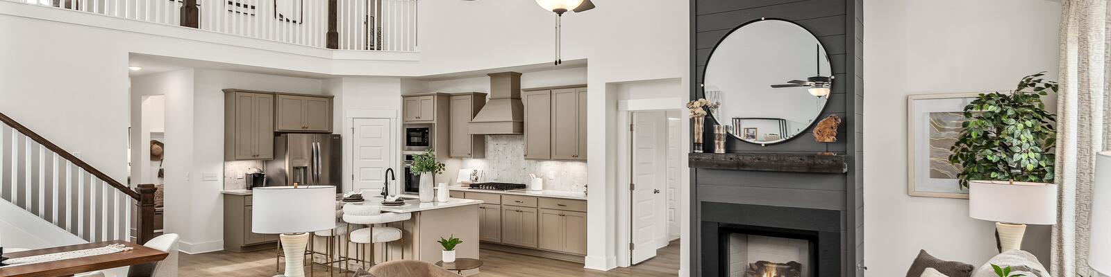 Spacious modern living room with white walls, open white kitchen, light gray sofa with green pillows, glass coffee table, har