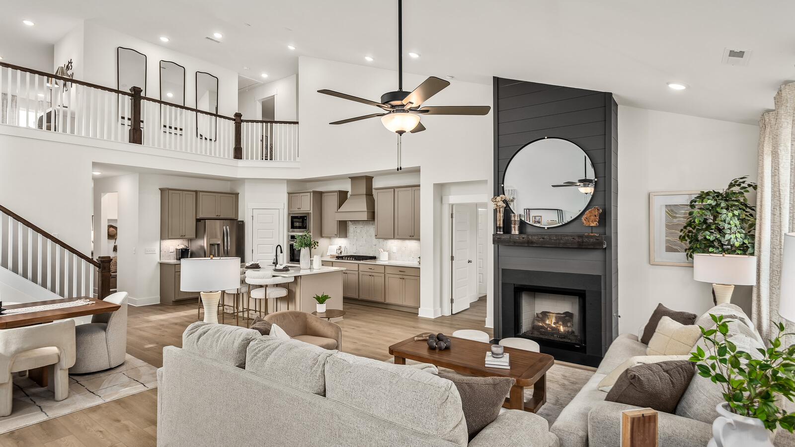 Spacious modern living room with white walls, open white kitchen, light gray sofa with green pillows, glass coffee table, har