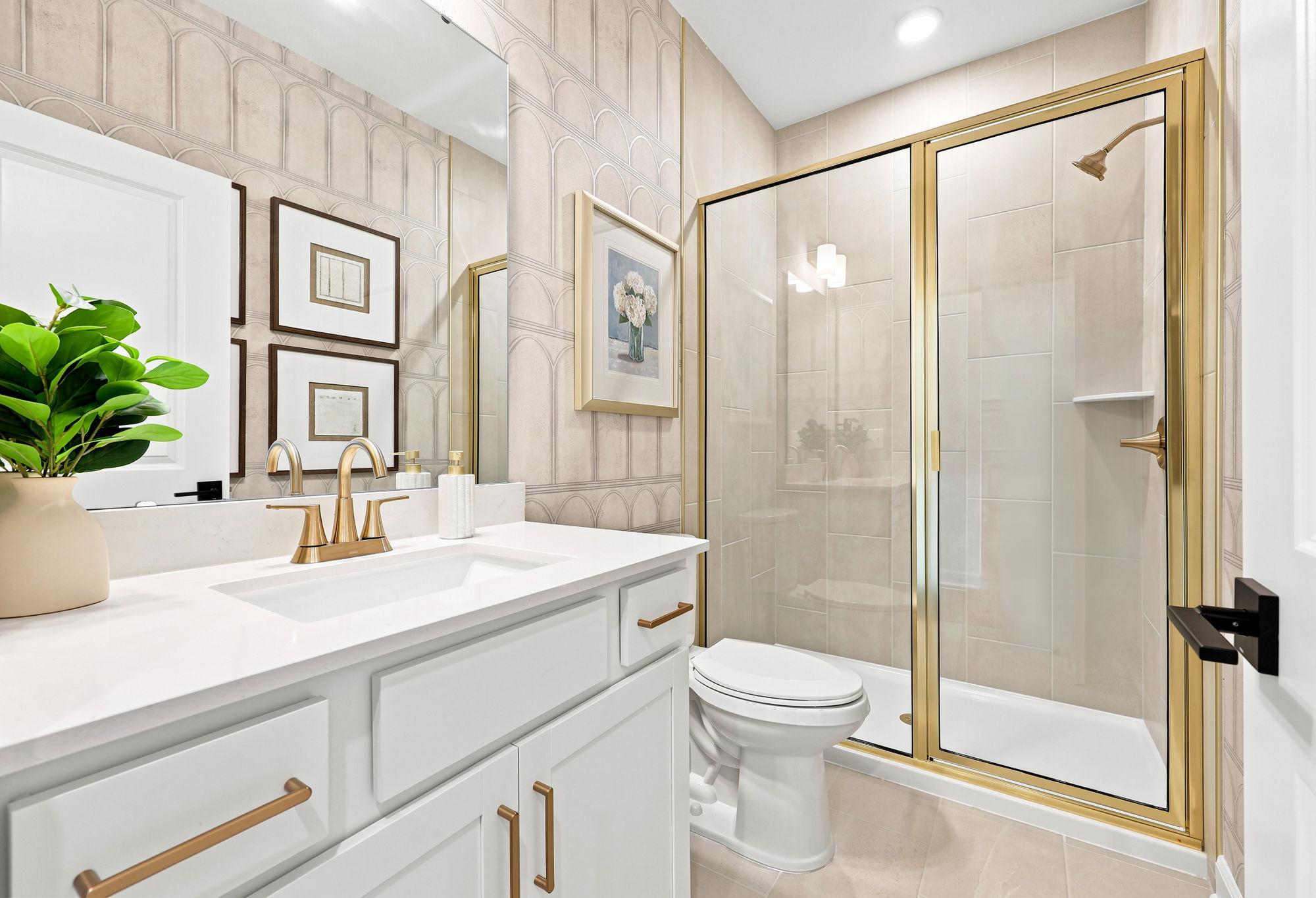 Modern bathroom in The Beech by Davidson Homes featuring a white vanity, gold fixtures, and a glass-enclosed walk-in shower.