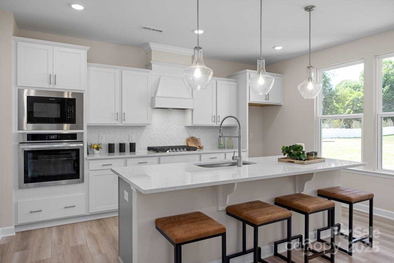 Modern white kitchen with shaker cabinets, stainless double oven, gas cooktop, quartz island, and pendant lights in Davidson Homes The Chestnut F, Belmont, NC
