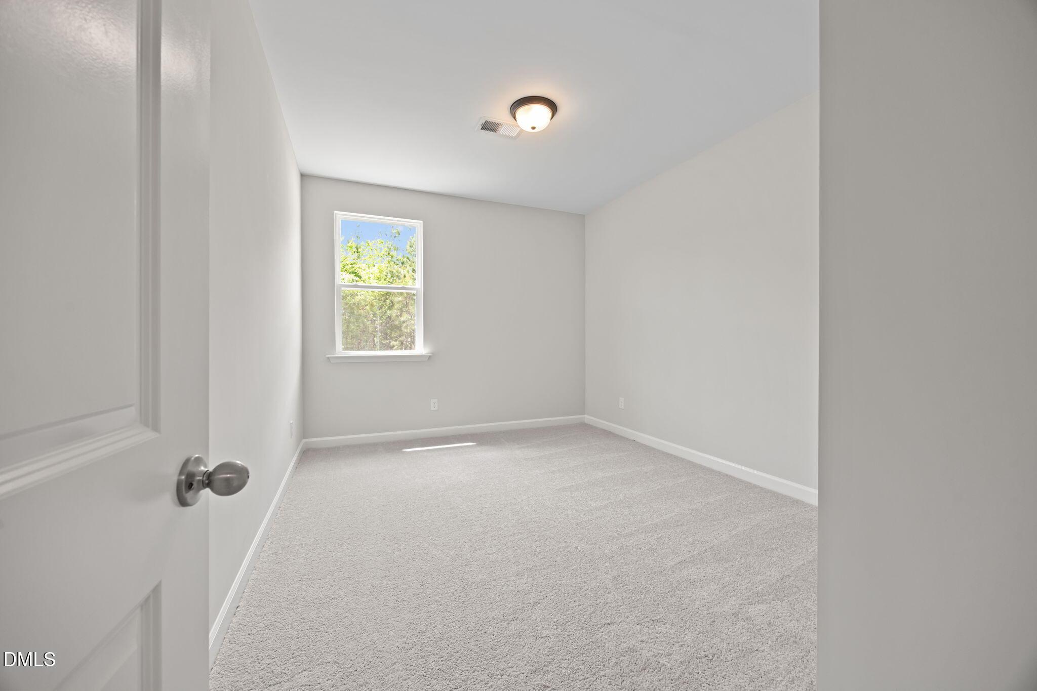 Empty bedroom with light gray walls, beige carpet, large window with greenery view in Davidson Homes The Willow D, Wendell, NC
