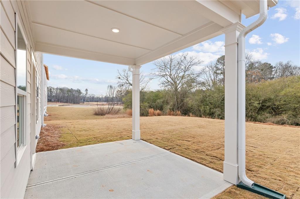 Covered side patio with white columns on two-story beige home overlooking wooded yard in Cedar Farms, Winder, Georgia