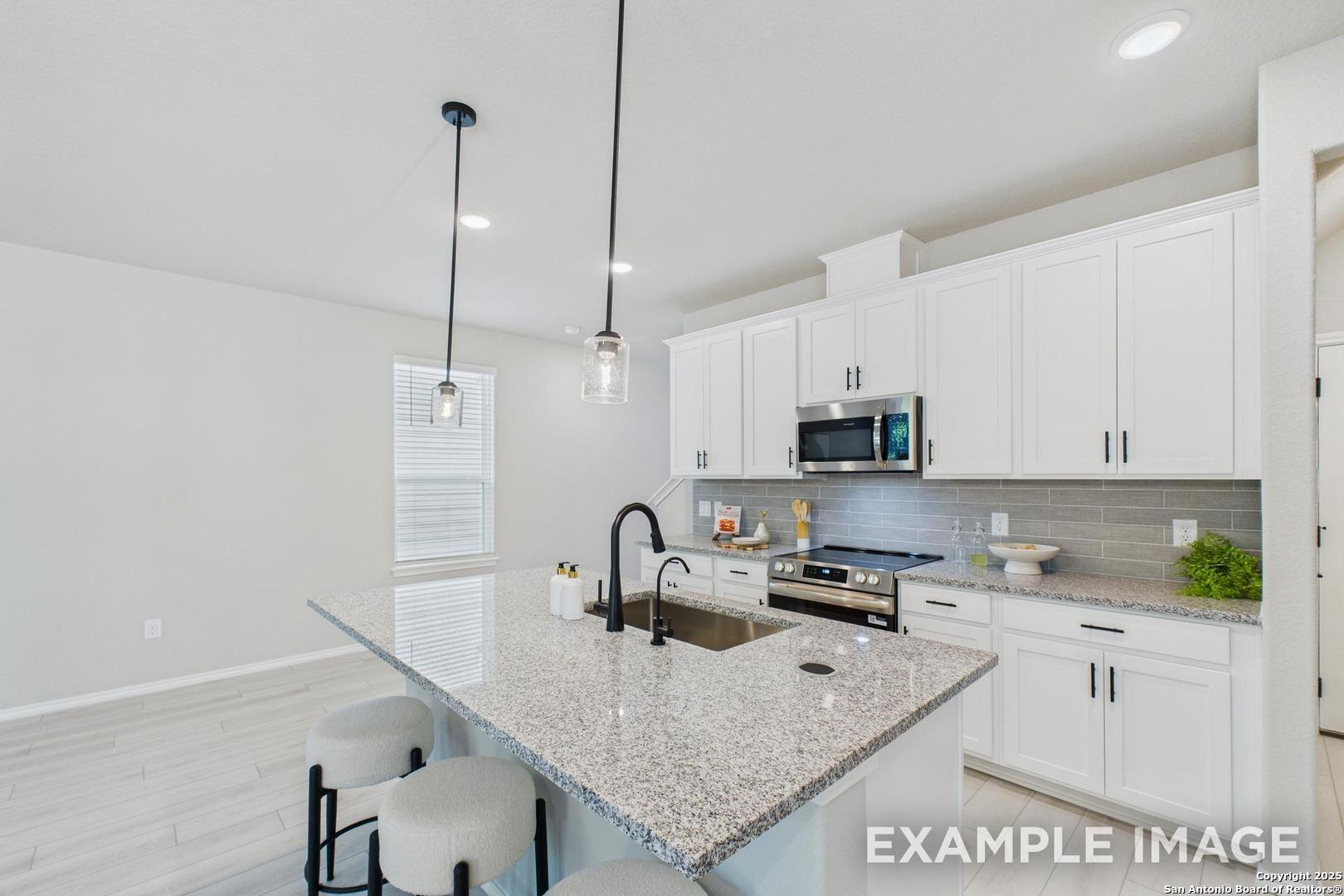 Modern kitchen with granite island, white cabinets, stainless appliances, and pendant lights in The Charlotte B, San Antonio, Texas